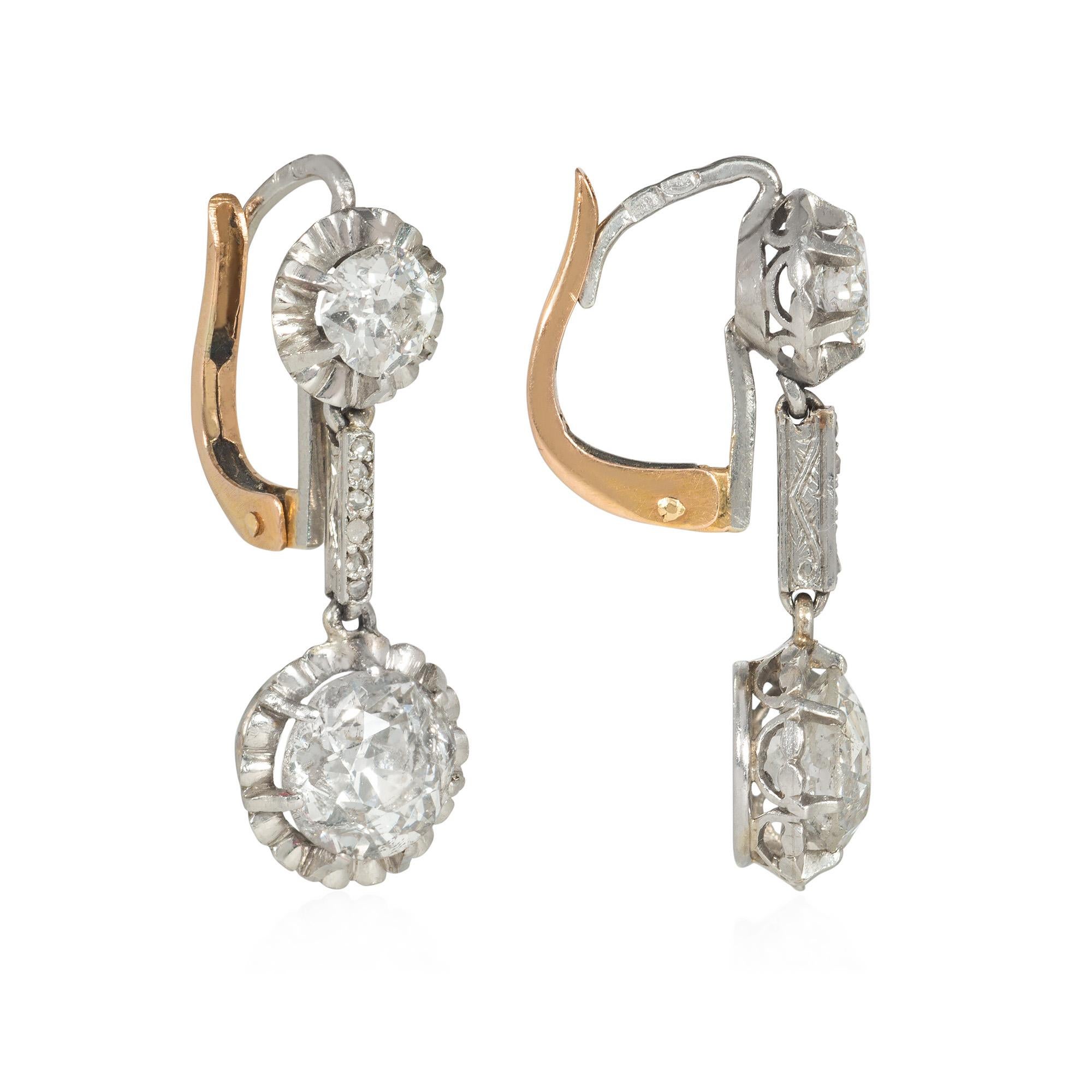A pair of Art Deco two-stone diamond drop earrings of dormeuse style, comprised of old European-cut diamonds in ruffled settings with a bar spacer and lever back, in platinum and 18k gold. French import.  Atw diamonds 2.40 cts.; two surmounts