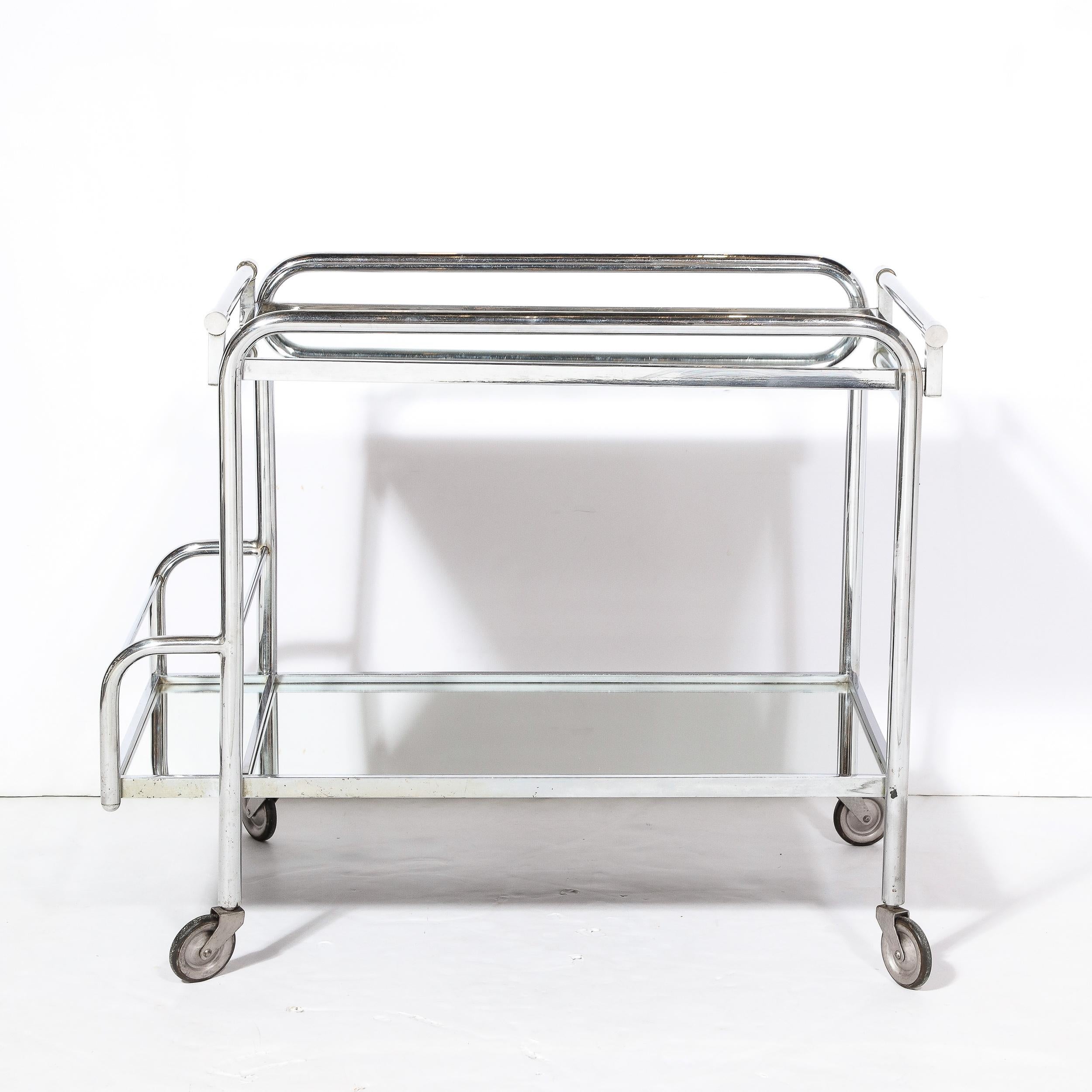 This elegant and sleek Art Deco Machine Age Two-Tier Bar Cart in Chrome and Mirror  was made by Jacques Adnet and originates from France, Circa 1935. Composed in looking rods of chrome composing the frame of the piece, the proportions and minimal