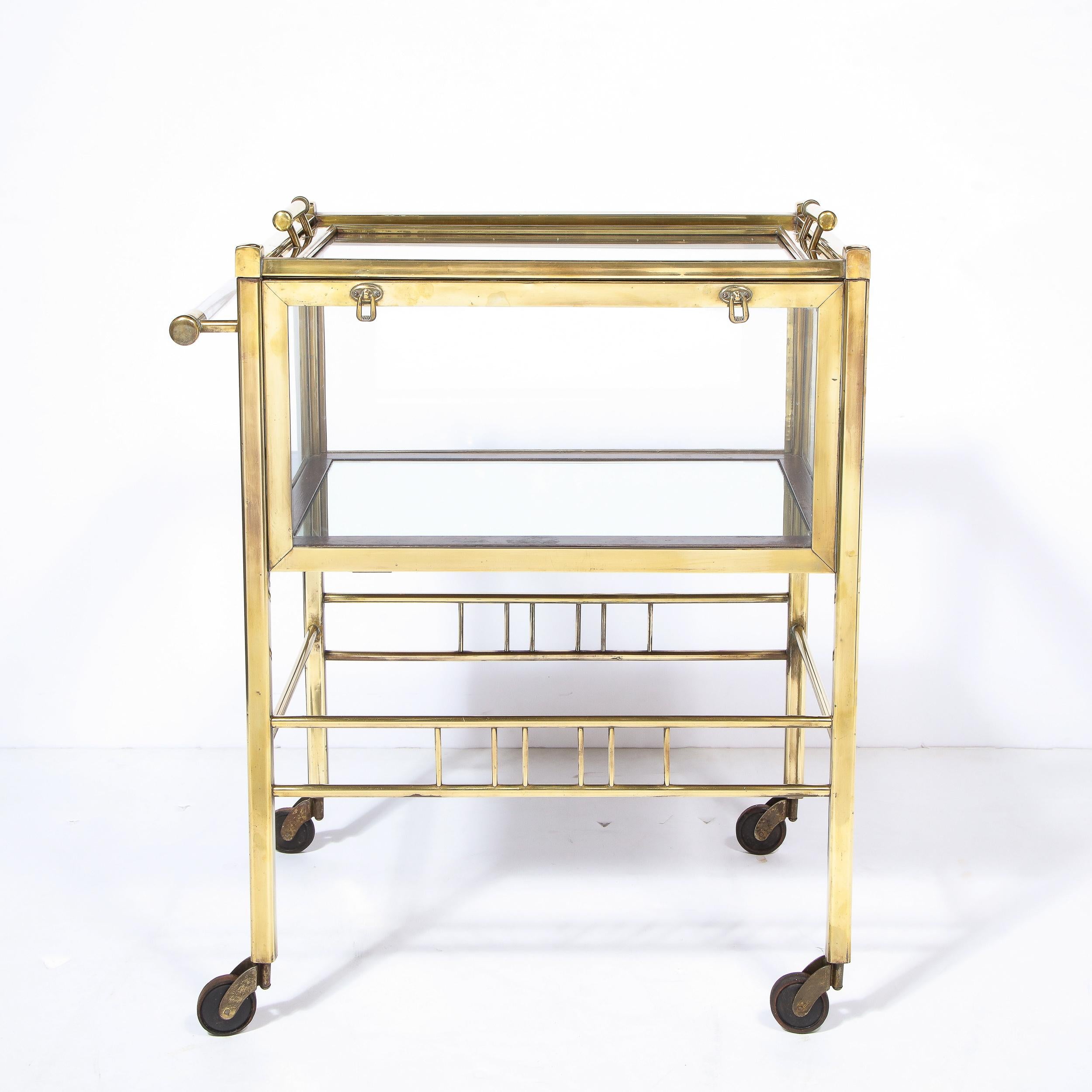 This stunning Art Deco bar cart was realized in Germany, circa 1925. Composed of lustrous polished brass, it offers a volumetric rectangular body with two tiers of translucent glass; a removable top with two cylindrical brass handles; and a bottom