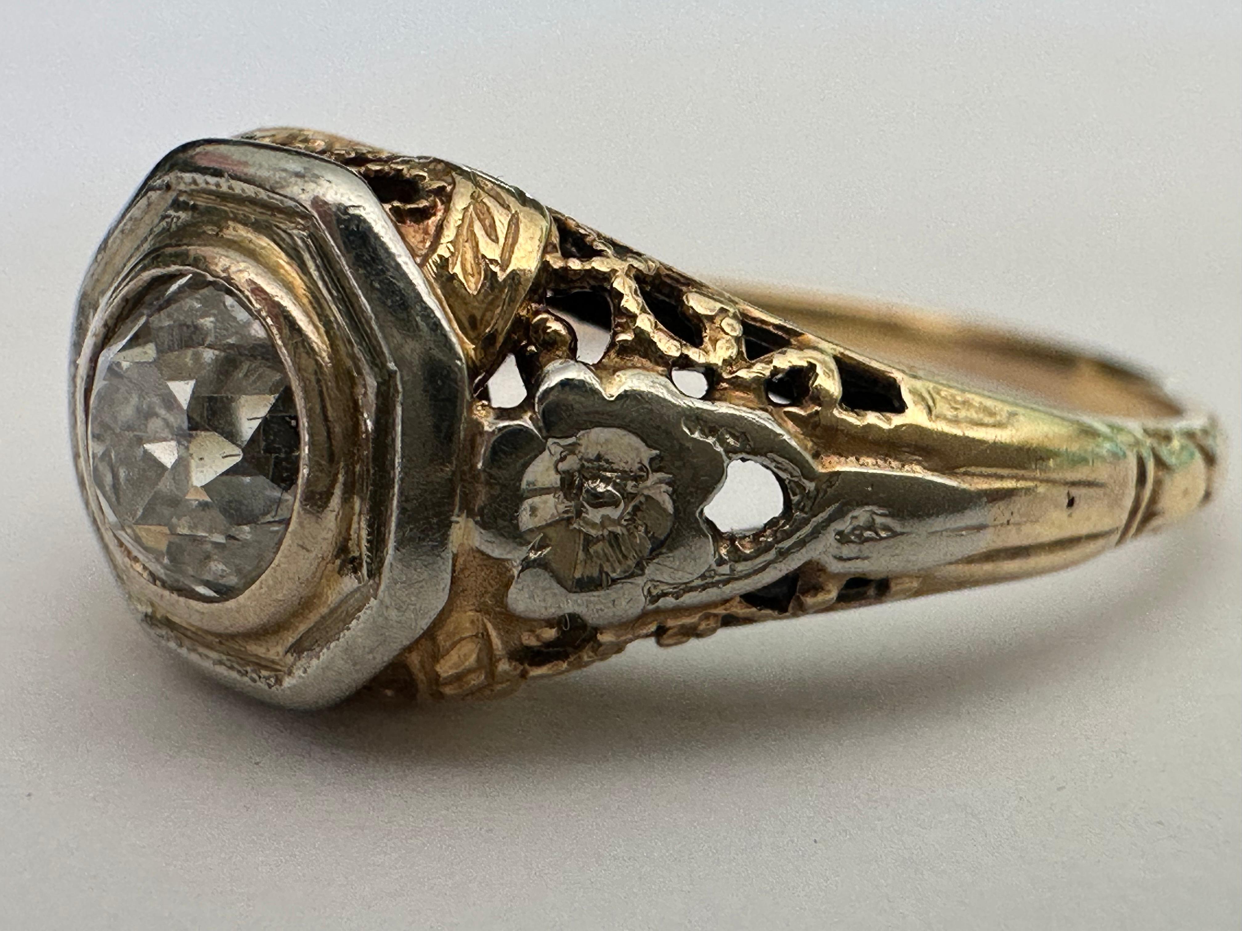 Un diamante di taglio europeo antico di circa 0,55 carati, di colore I-J e purezza SI1, è al centro di questo antico anello solitario bicolore impreziosito da un piercing decorativo e da una raffinata filigrana. Incastonato in oro bianco e giallo 14