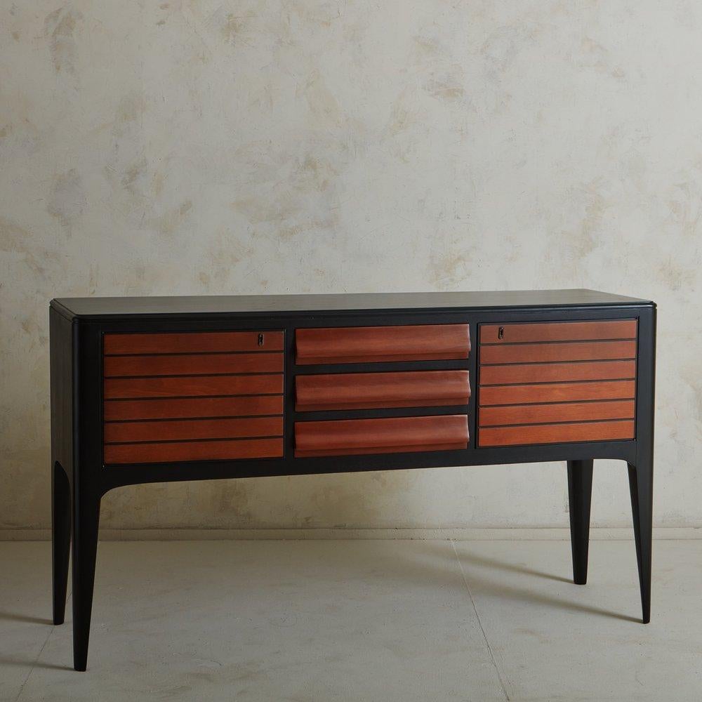 A vintage Italian Art Deco style credenza featuring an ebonized wood frame with angular lines and tapered legs. It has two cabinets with linear stripe details and three center drawers with subtle curves and built-in handles. It has a lacquered