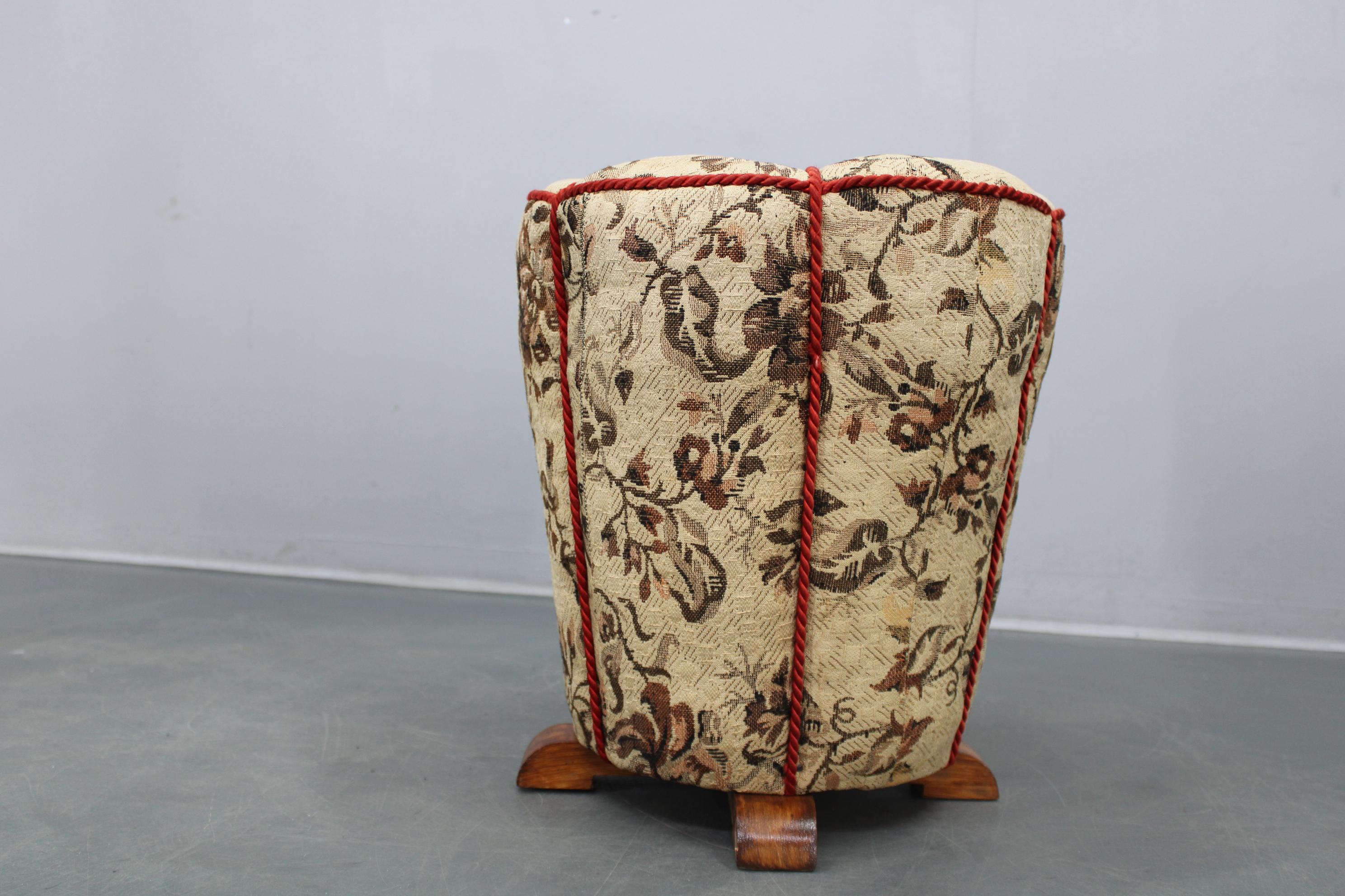 Elegant Art Deco upholstered stool produced in Czechoslovakia during the 1930s. The piece features a robust wooden internal structure, padded upholstery, and a decorative floral textile trimmed with original red piping. The rounded, segmented body