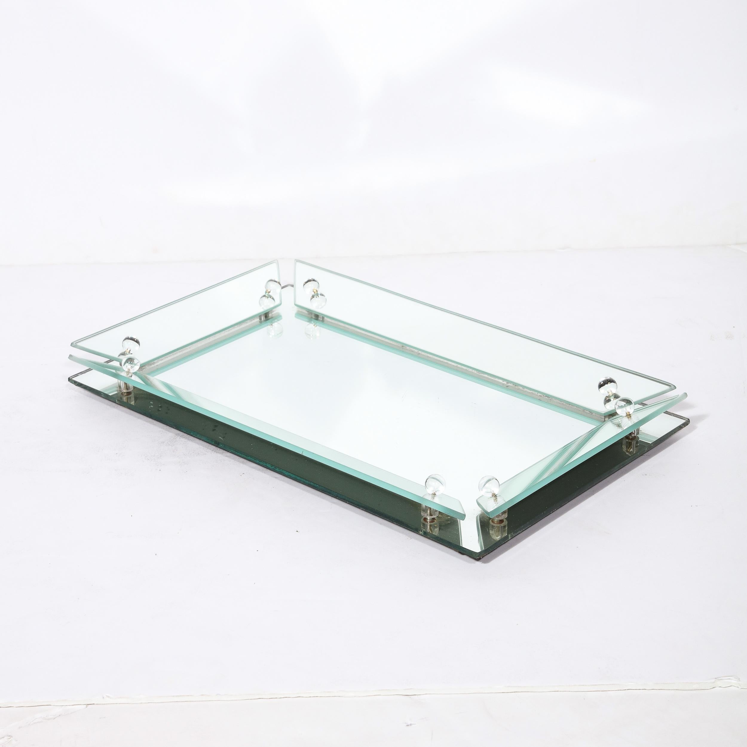 This elegant Art Deco Vanity Tray originates from the United States, Circa 1935. Composed in cut and beveled mirror glass, the border of the tray angles inwards and is composed of spaced rectilinear elements attached with glass studs, two on each