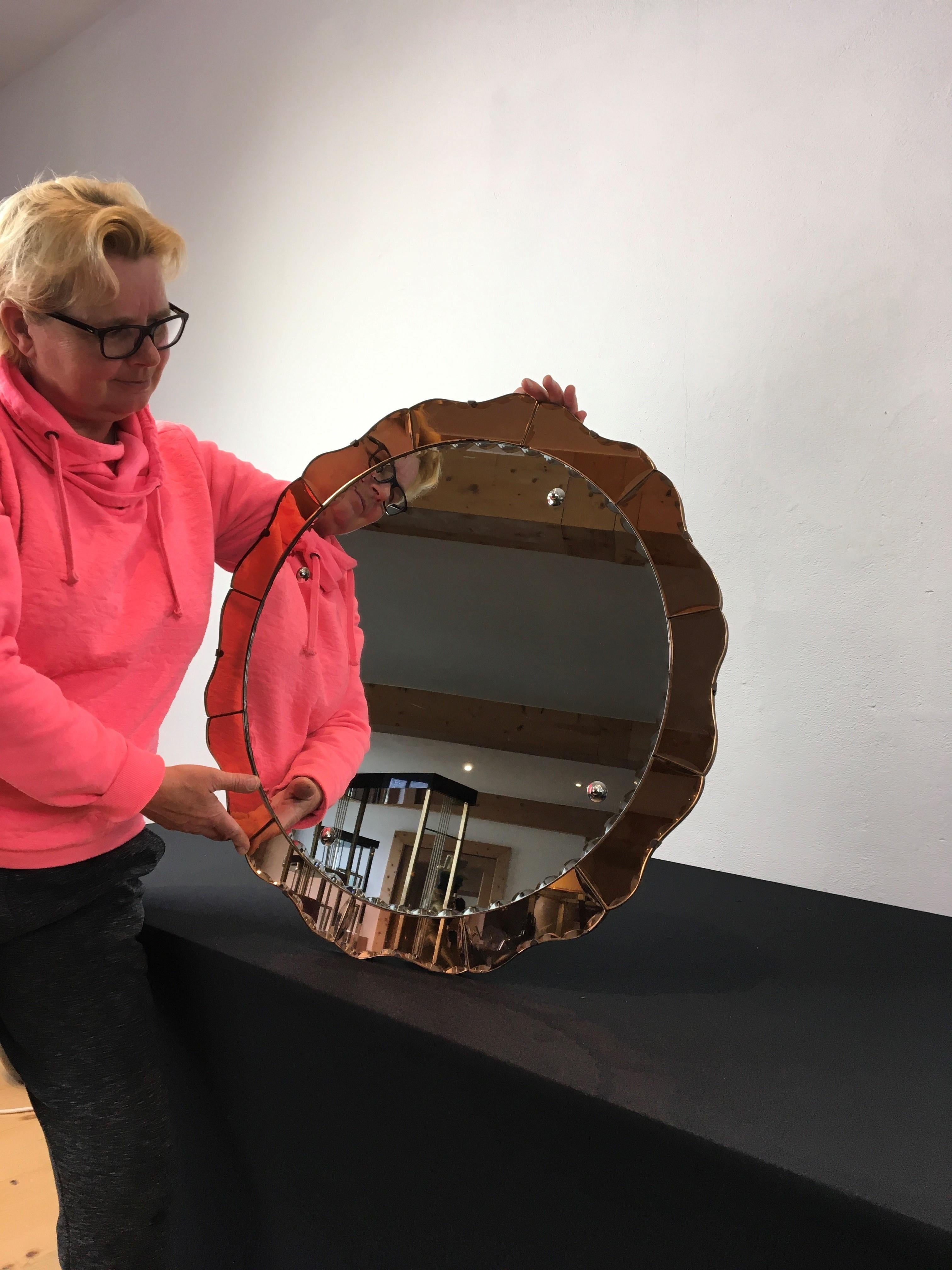 Art Deco Venetian wall mirror. 
A 1930s two-tone round mirror with curves. 
Around the mirror glass you have old pink - rose - peach mirror glass. 
As well the central mirror glass as the colored mirrror glass have a faceted edge all around, in