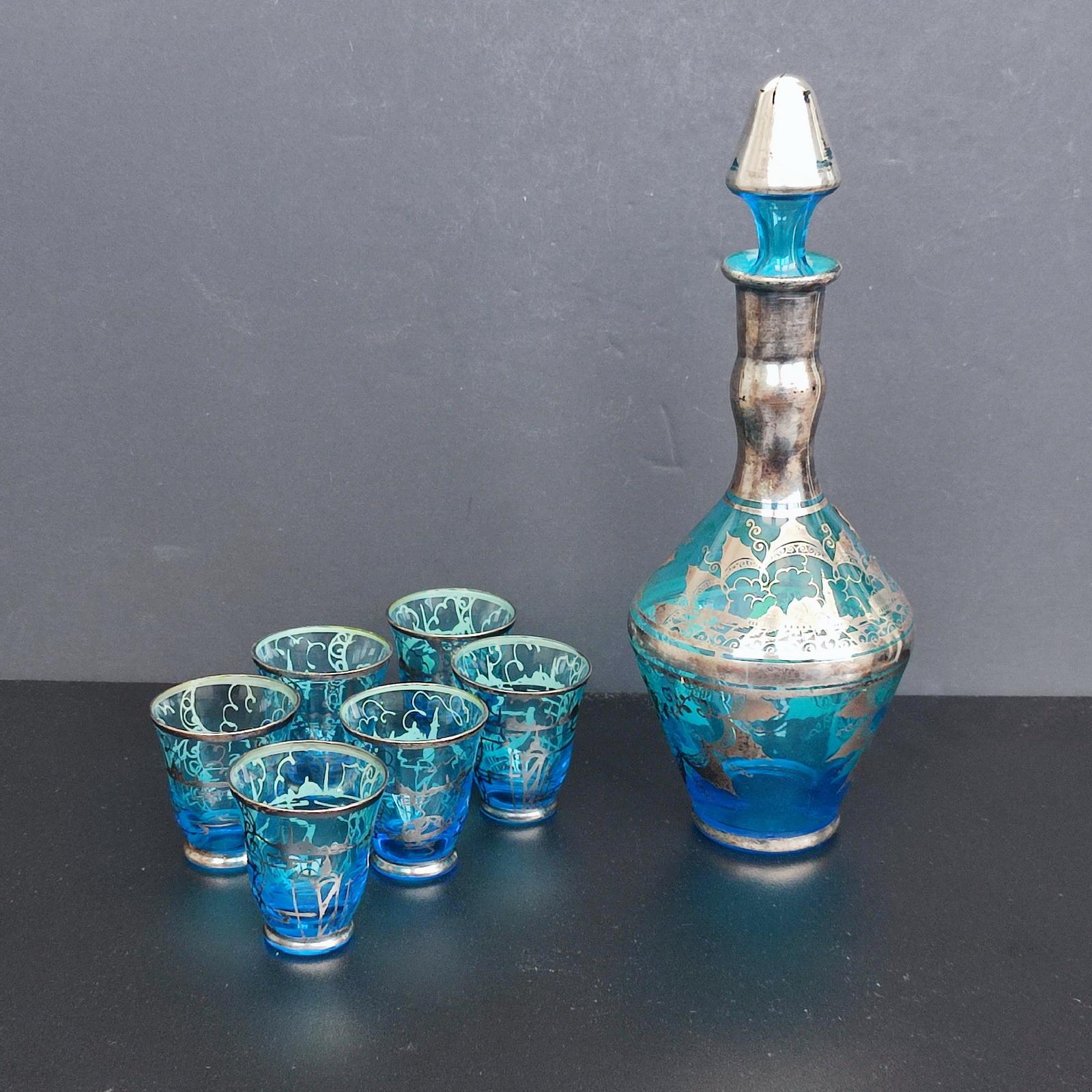 A fine vintage Venetian, Murano blue glass liquor decanter with stopper and six matching shot glasses. Each applied with a sterling silver overlay, decorated with the San Giorgio landscape. The glasses are similarly decorated. The decanter retains