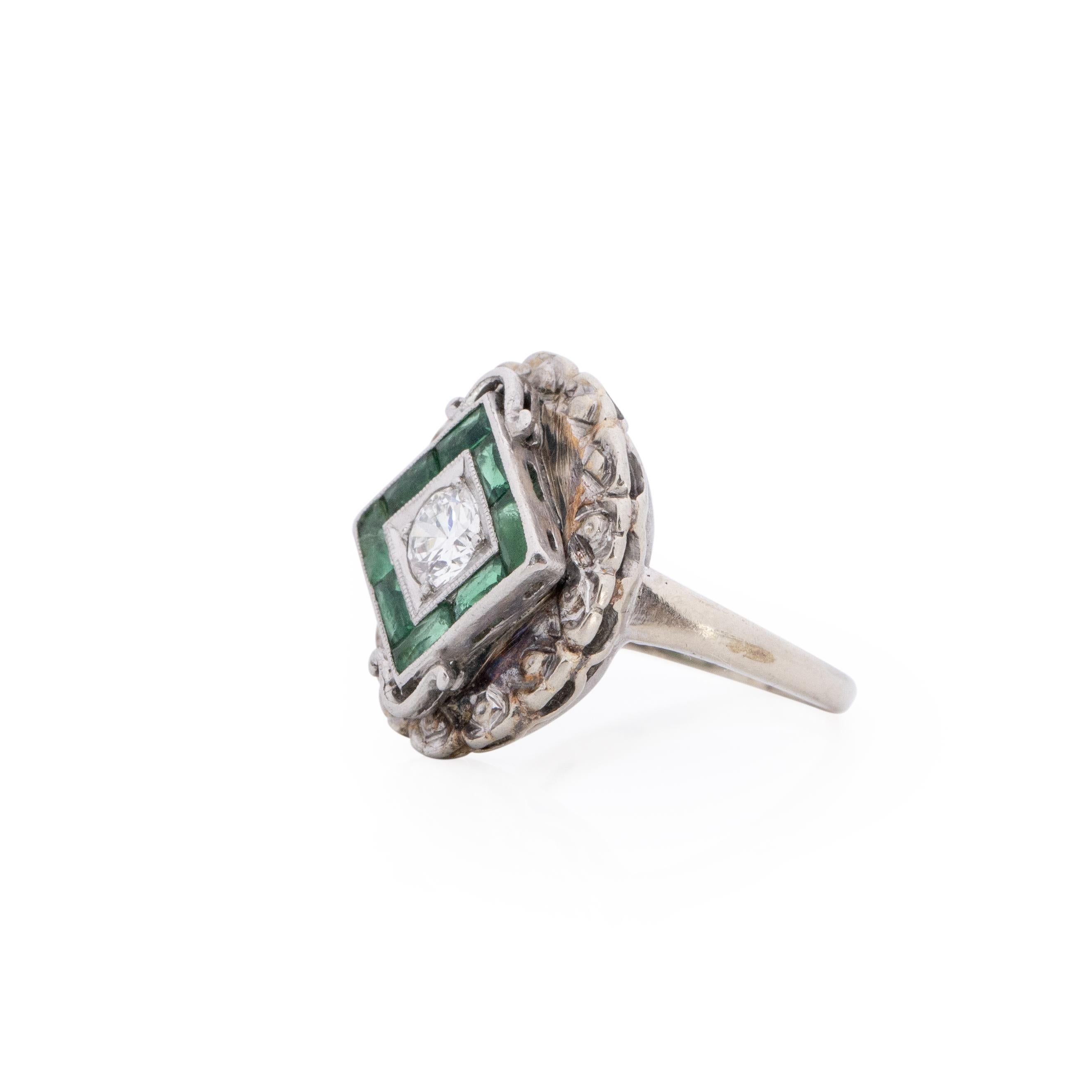 This art deco piece has a beautiful regal edge. Crafted in 10K white gold, in the center of a square baguette emerald halo is a beautiful old European cut diamond. The final details are the scalloped design rounding out the whole small oval shield