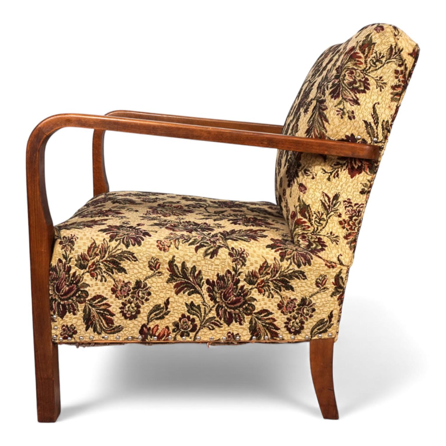 Un sillón Art Déco con un motivo floral excepcional. La tela ocre claro presenta un diseño con flores y hojas lilas. Se encuentra en muy buen estado. Los muelles del sillón son impecables y proporcionan una comodidad de asiento de buena a firme. Los