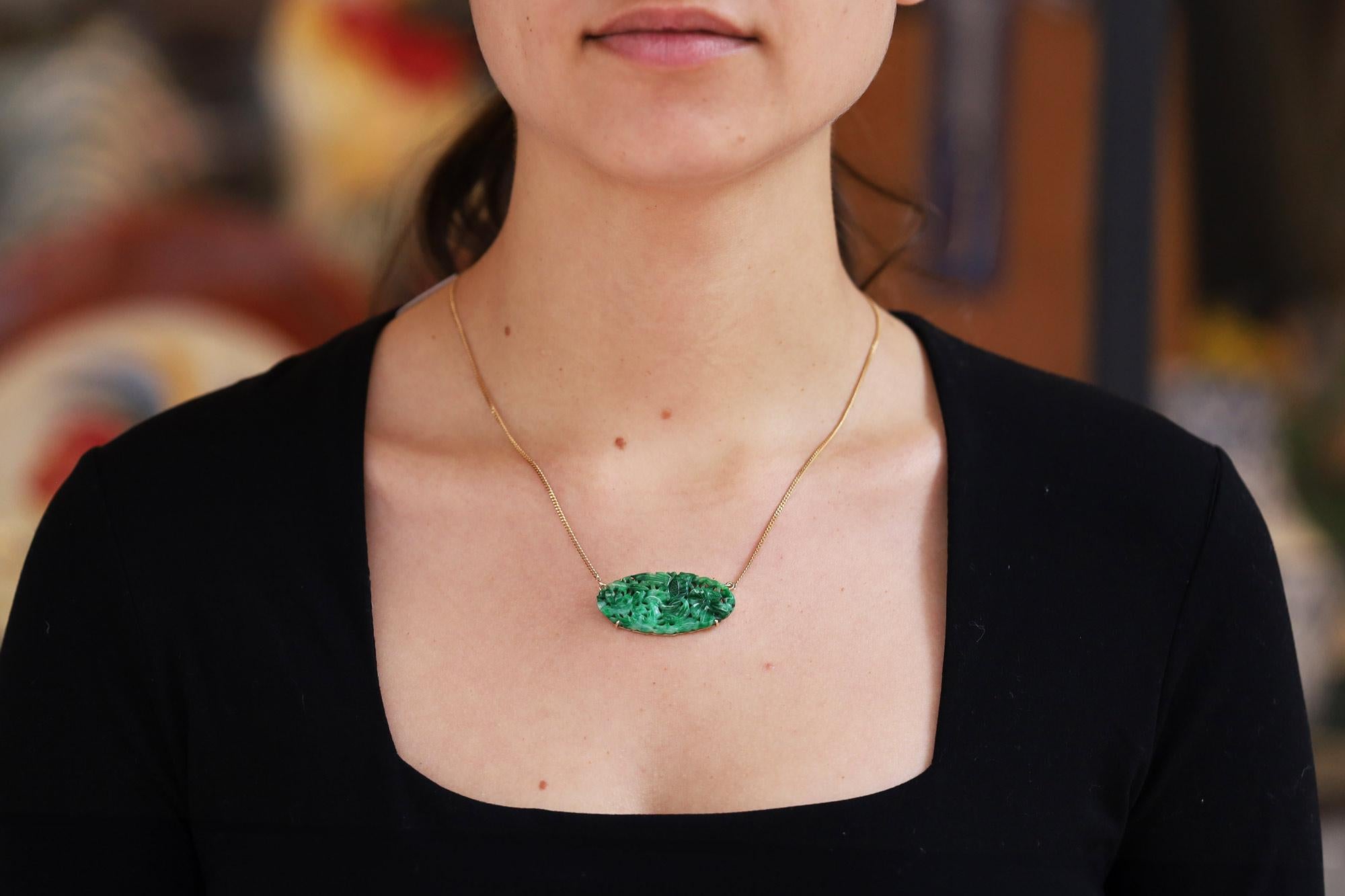 A vintage and verdant natural jadeite jade pendant necklace playfully set in an East-West orientation. The highly detailed floral plaque featuring a deeply carved reticulating surface bursting with rich spinach and dark, apple-green tones. This