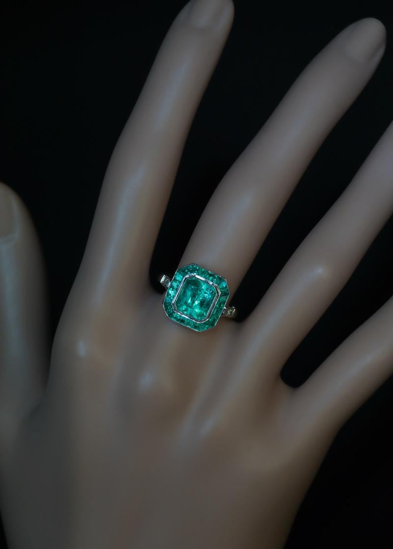 This Art Deco vintage 18K white gold ring was made in Czechoslovakia in the 1920s. The ring is centered with a sparkling bluish green emerald cut emerald measuring 7.68 x 7.09 x 5.6 mm (approximately 2.11 ct). The centerstone is framed by well