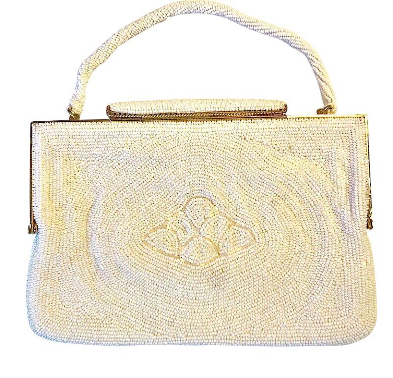 This Vintage Art Deco women’s evening bag has stylized patterns of white beaded waves. It has a white beaded rope handle. The frame is gold metal with a gold metal clasp. The interior is silk with a pocket for accessories such as the small leather