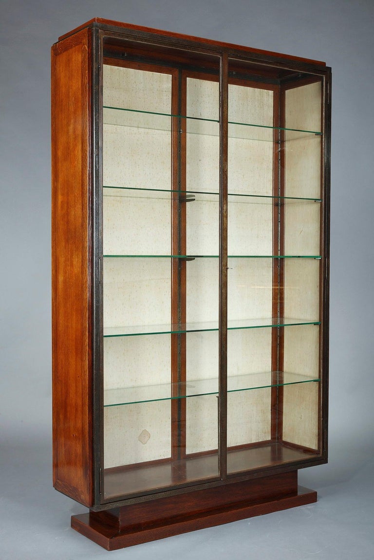 Large Art Deco display case from 1930, by Charles Dudouyt in wood and gunmetal frame, opening with two glass doors and including five glass shelves. The base rests on a wooden pedestal and the interior walls of the cabinet are covered with a cream