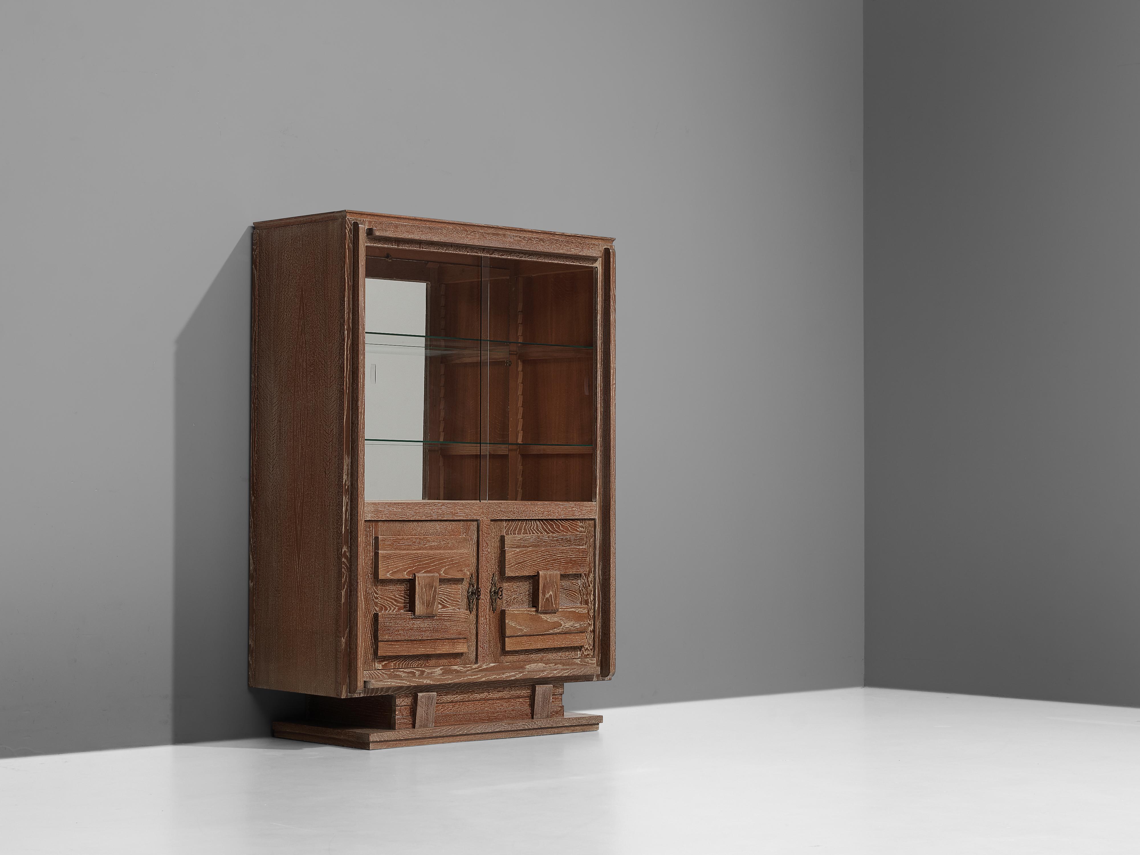 Cabinet, in glass and oak, France 1940s. 

Nice detailed cabinet in cerused oak with glass vitrine sliding-doors. The high storage part consists of a vitrine part, with two glass shelves and a mirrored back. The lower part is a cabinet with two
