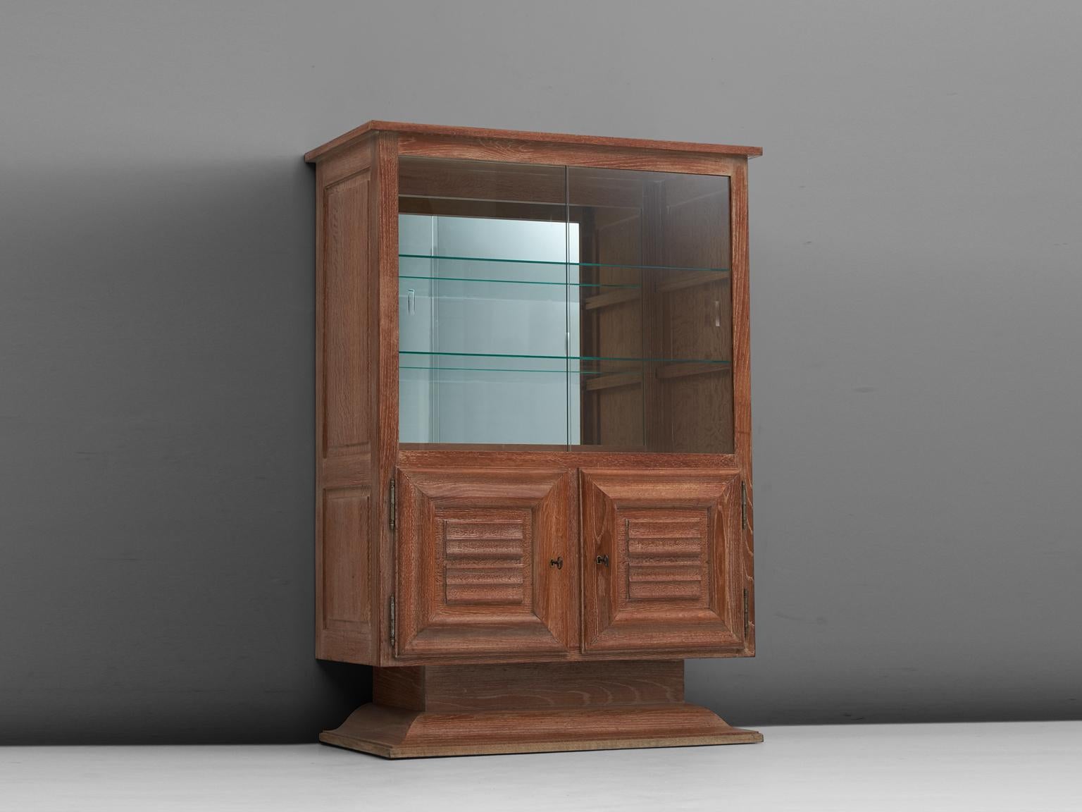 Cabinet, in glass and oak, France, 1950s. 

Nice detailed cabinet in cerused oak with glass vitrine sliding-doors. The high storage part consist of a vitrine part, with two glass shelves and a mirrored back. The lower part is a cabinet with two