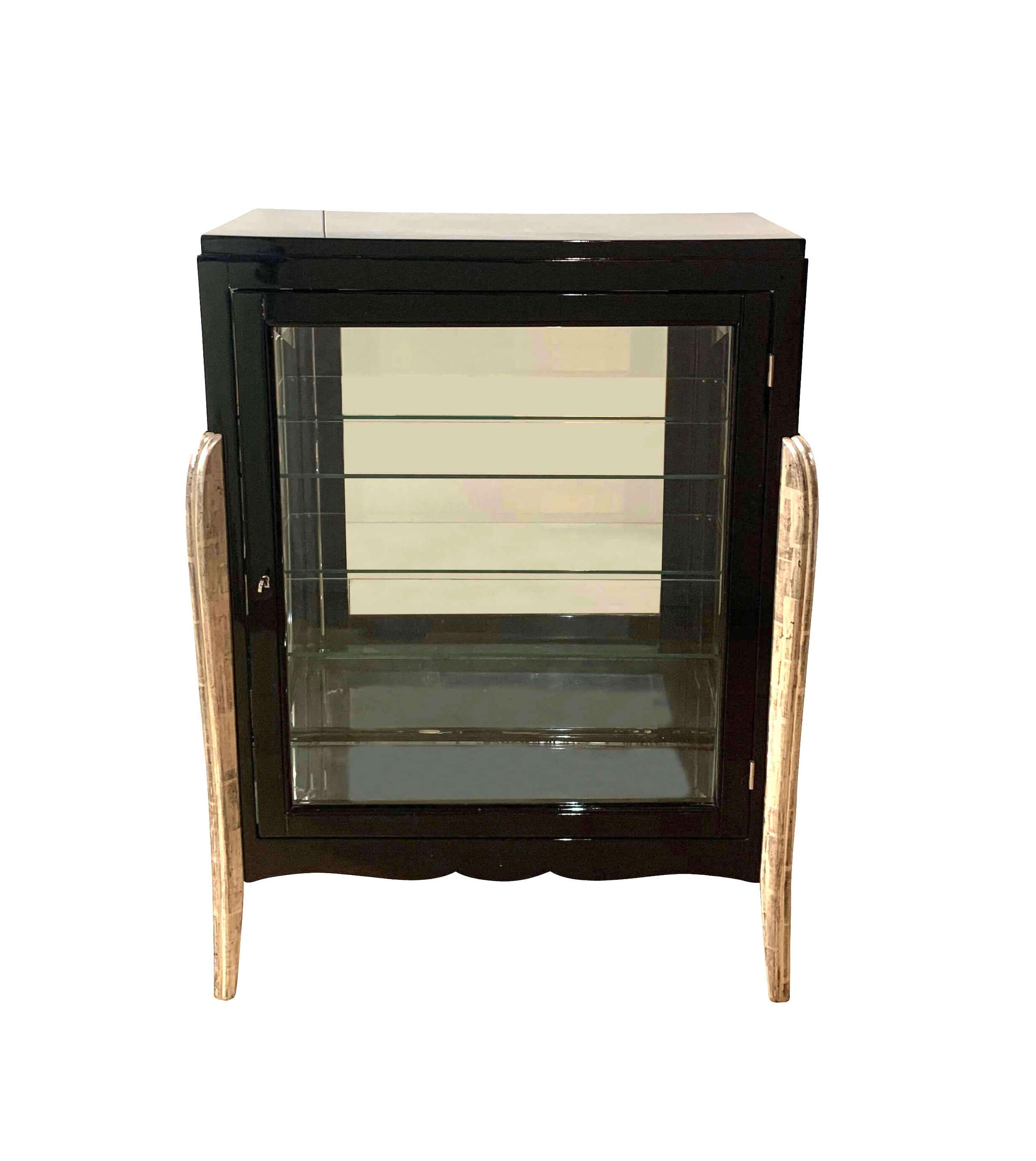 Small, elegant, restored Art Deco Showcase / Vitrine from France about 1930.

Black high-gloss piano lacquer on wood. Standing on four silver-colored, curved and fluted legs. Three sides glass with two glass shelves. 
At the bottom and back with