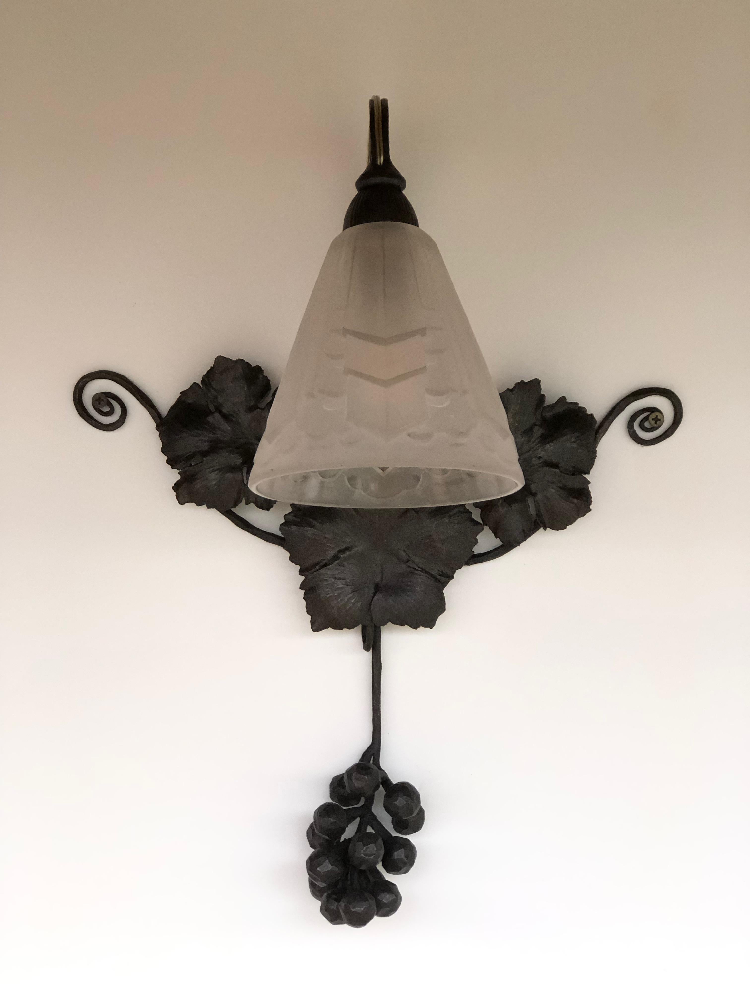 Art deco wall lamp around 1930, in the style of Degue.
Wrought iron frame decorated with vine leaves and bunches of grapes. 
Molded glass tulip with geometric decoration.
Wall lamp in perfect condition and electrified.
For more information do not