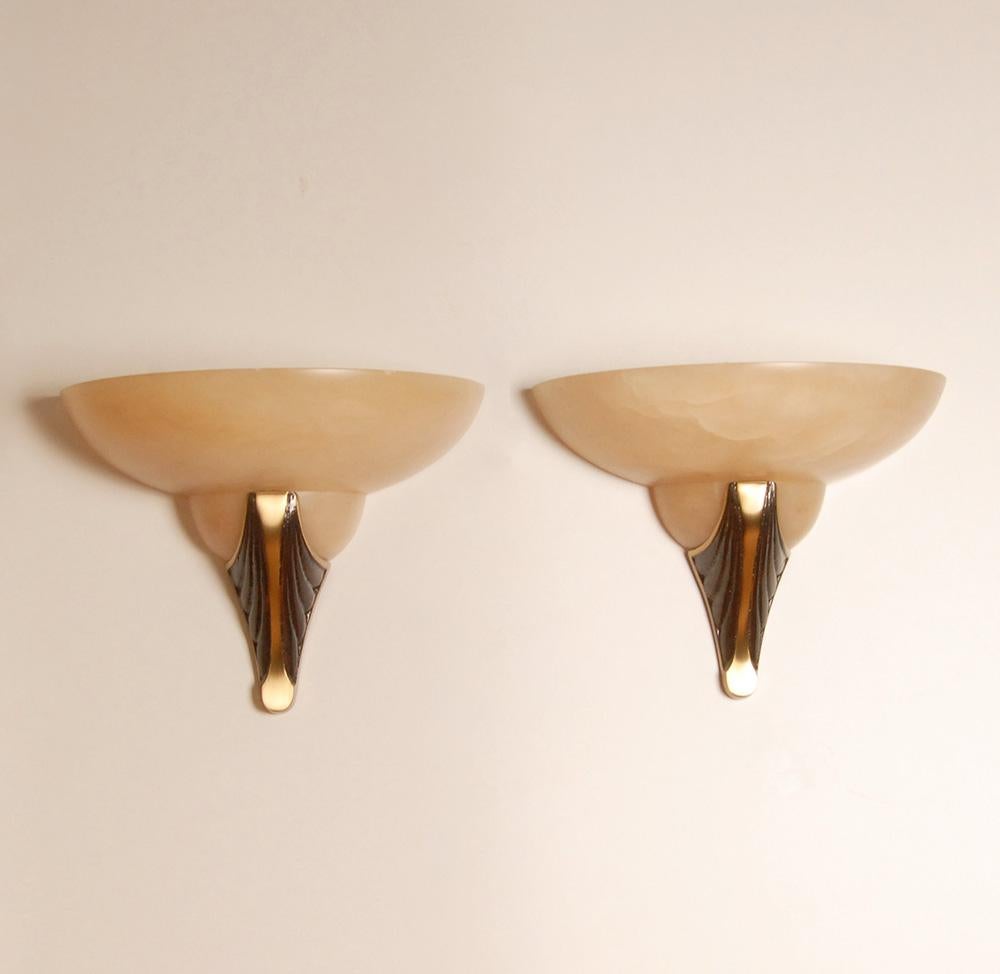Lampade da parete del Mid Century Art deco Revival.
Realizzato in alabastro marmoreo dall'aspetto torbido.
Il paralume in marmo poggia su un elegante elemento a forma di torcia in bronzo a due toni.
Il materiale in marmo naturale garantisce una luce