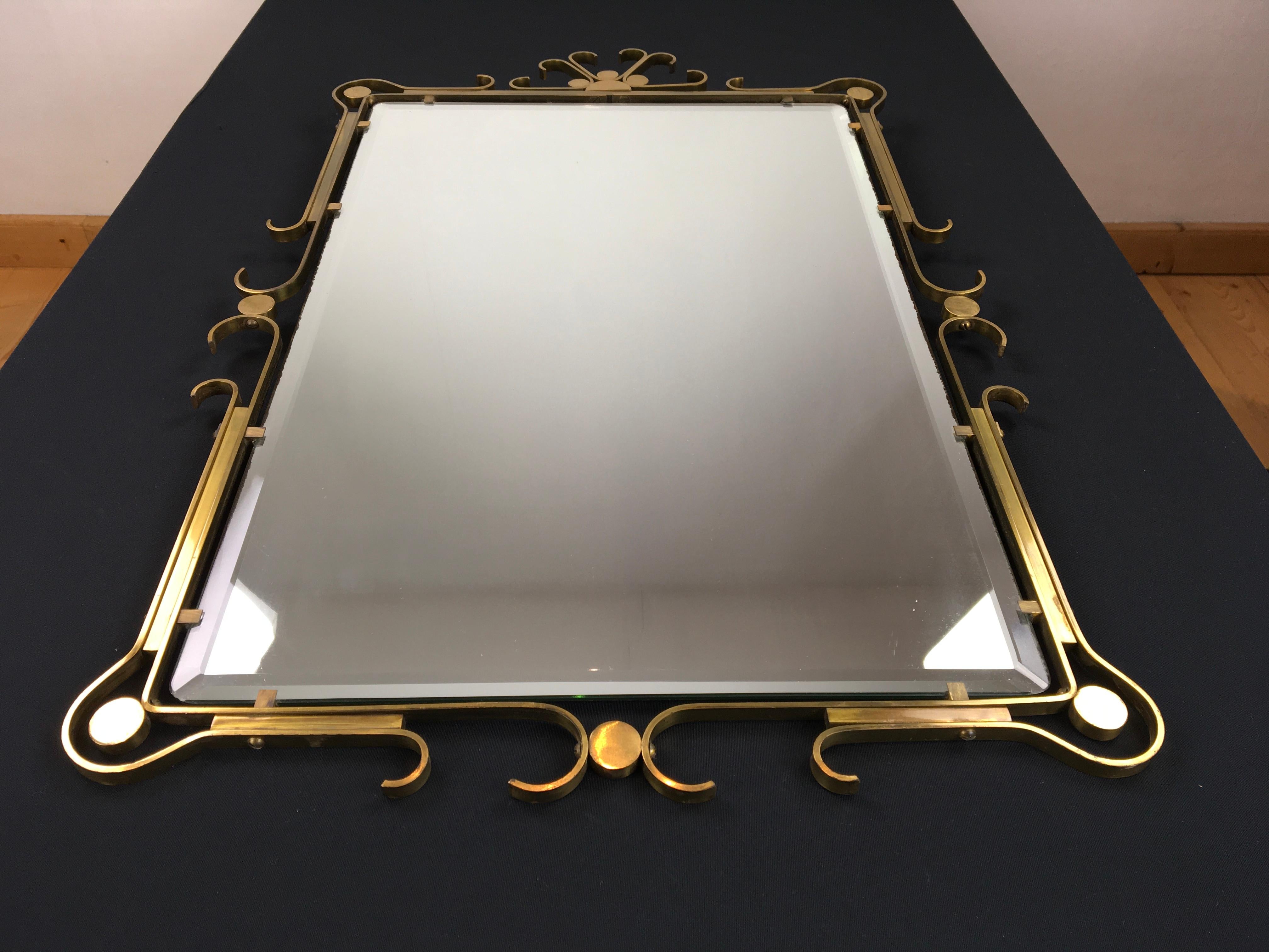 Brass wall mirror of the late Art Deco period, circa 1950s.
The brass or copper framework of this rectangular mirror has scrolled corners and is gracefully curved.
In the brass or copper frame you have the beveled mirror glass. 
The mirror glass