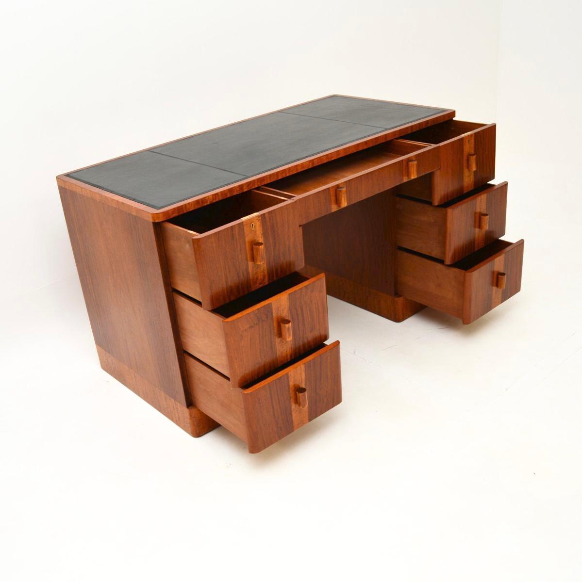 Magnifique bureau Art Déco en noyer et satiné avec dessus en cuir. Il a été fabriqué en Angleterre, il date des années 1930.

La qualité est exceptionnelle, la taille est impressionnante et le trou pour les genoux est généreux. Le design est