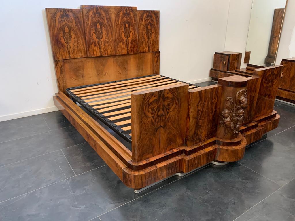 Art Deco bed and nightstand set probably made by the Ducrot firm of Palermo.
The wood is walnut in selection.
The bedside tables have a hinged door. The bed has a carved decoration on the front depicting festive putti. 
Dimensions H 140 x L 230 x