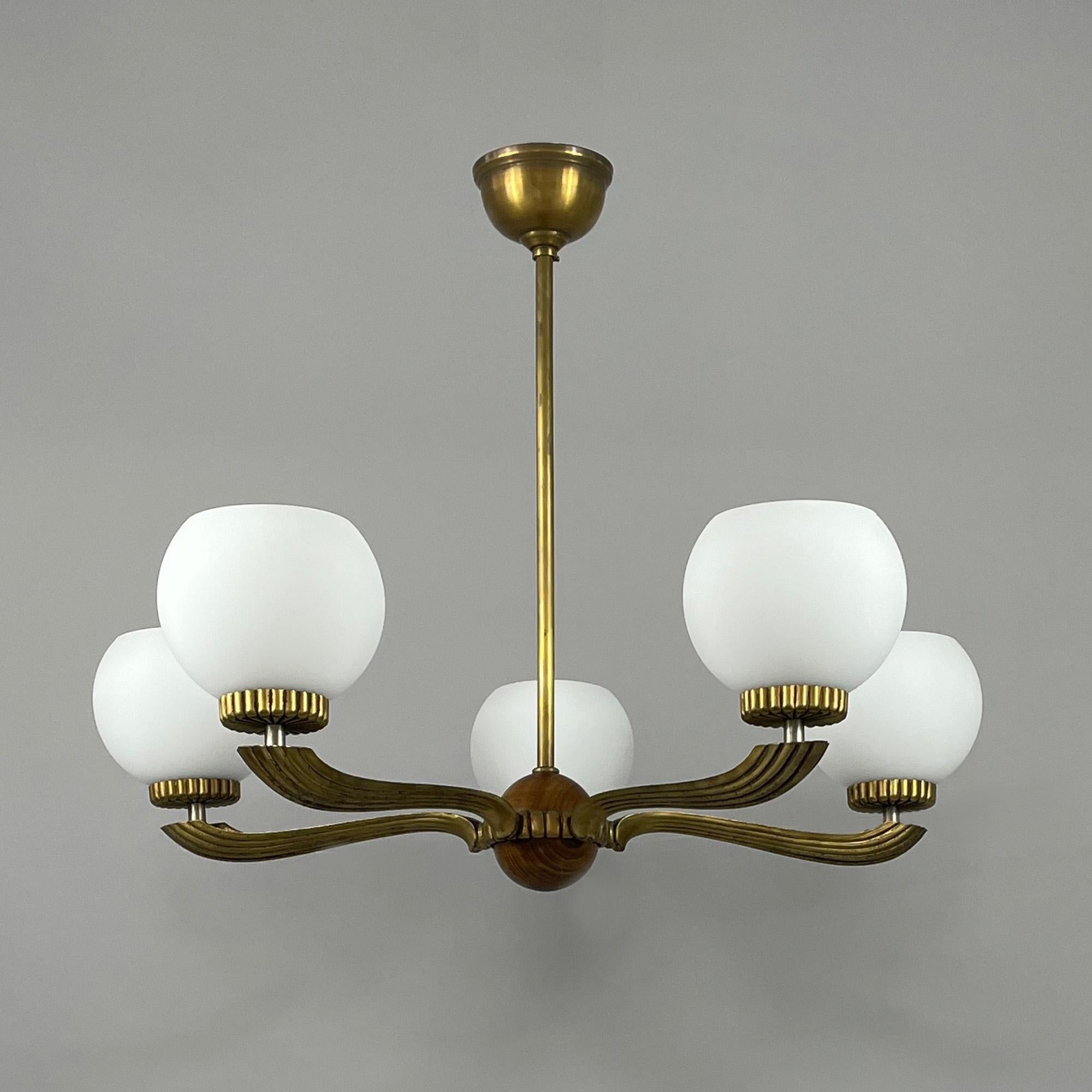 This elegant Swedish Grace Chandelier was designed and manufactured in Sweden in the 1930s during the Art Deco era. 

The light features a central brass rod, extending down to support a circular arrangement of five walnut curved arms. Each arm holds