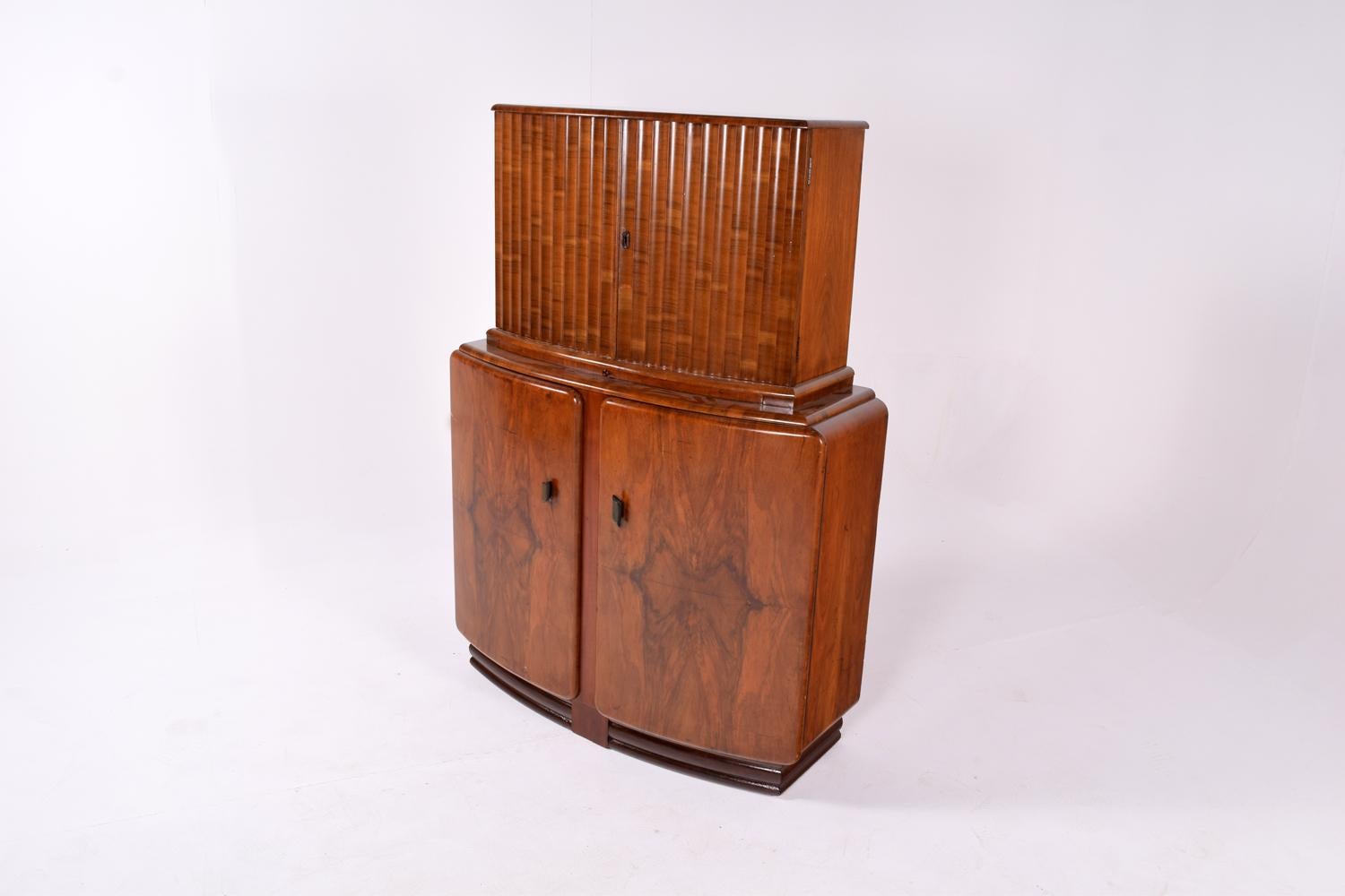 Gorgeous and original 1930s Art Deco cocktail cabinet in figured walnut. Originally from England and made by a company called 'Rivington'. This cocktail cabinet features a storage area for bottles. The top part of the cocktail cabinet has a mirrored