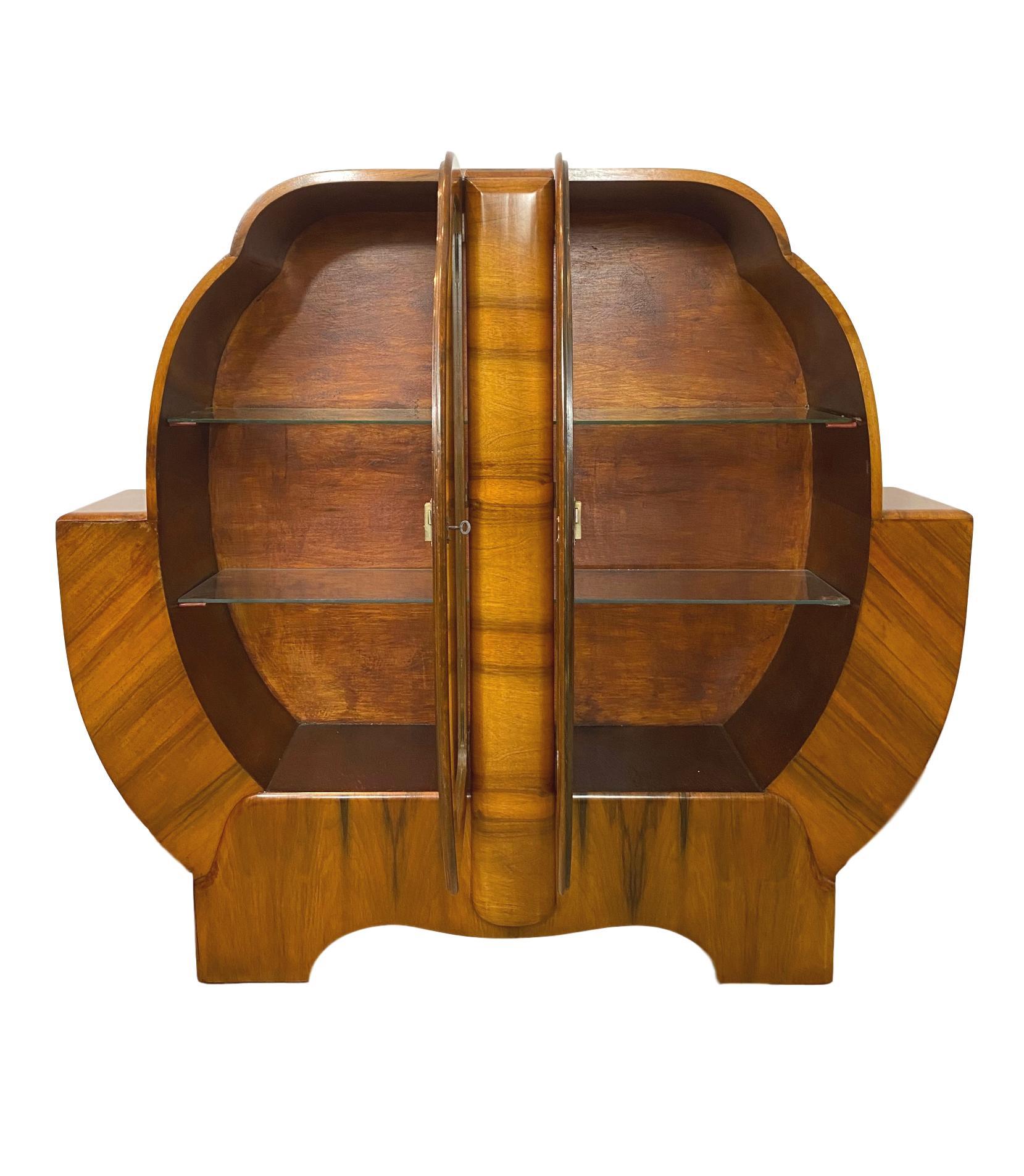 Mid-Century Modern Art Deco Walnut Display Case, English, ca. 1935, of cloud-shaped form, with a central molded pillar, with two 'butterfly' glazed doors, the interior with four glass shelves, the bottom half of the cabinet cradled by an