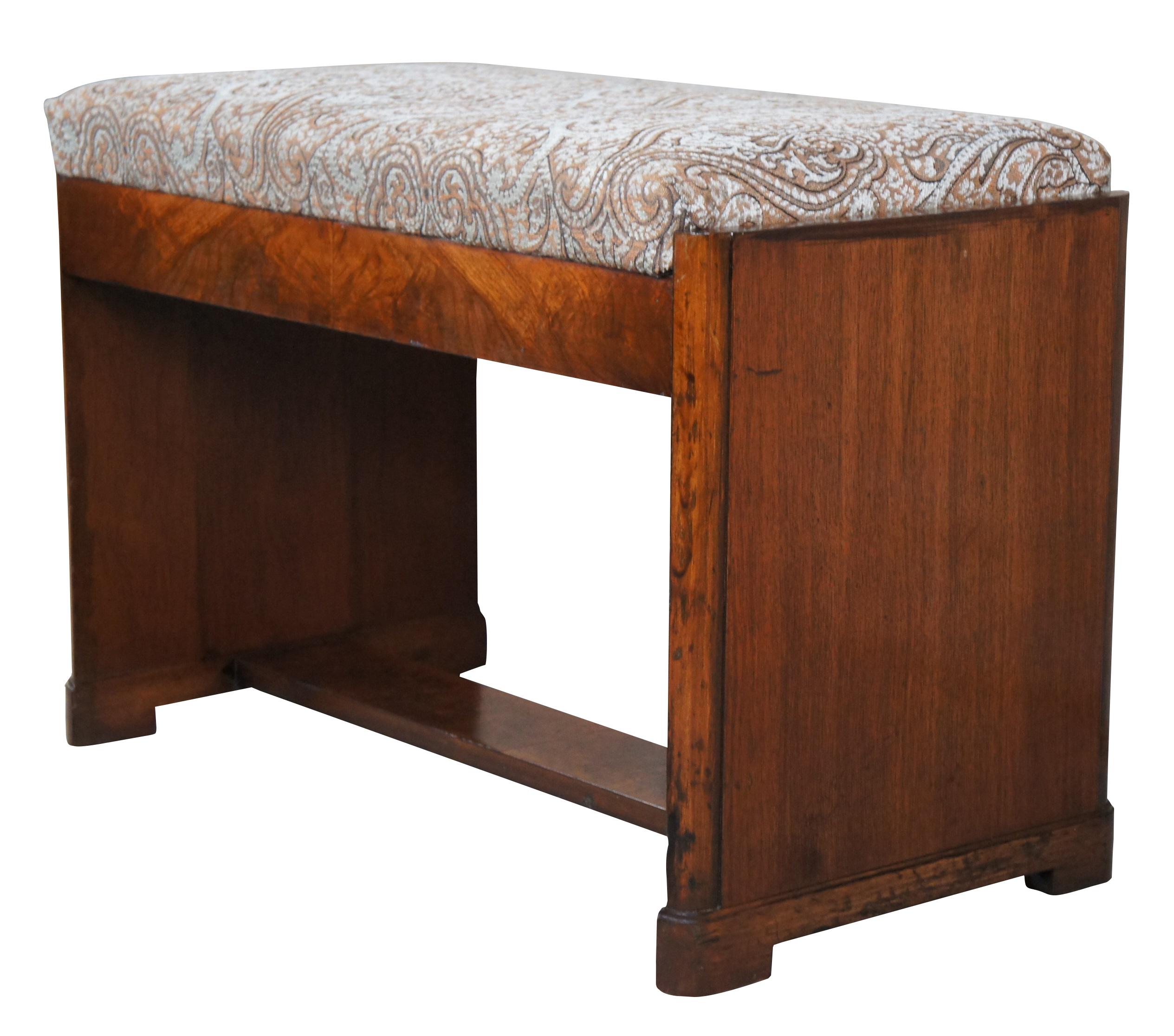A beautiful art deco vanity bench or piano stool. Made from walnut with matchbook veneer along the front. Features a trestle form with paisley upholstered top that opens to a divided storage compartment.

