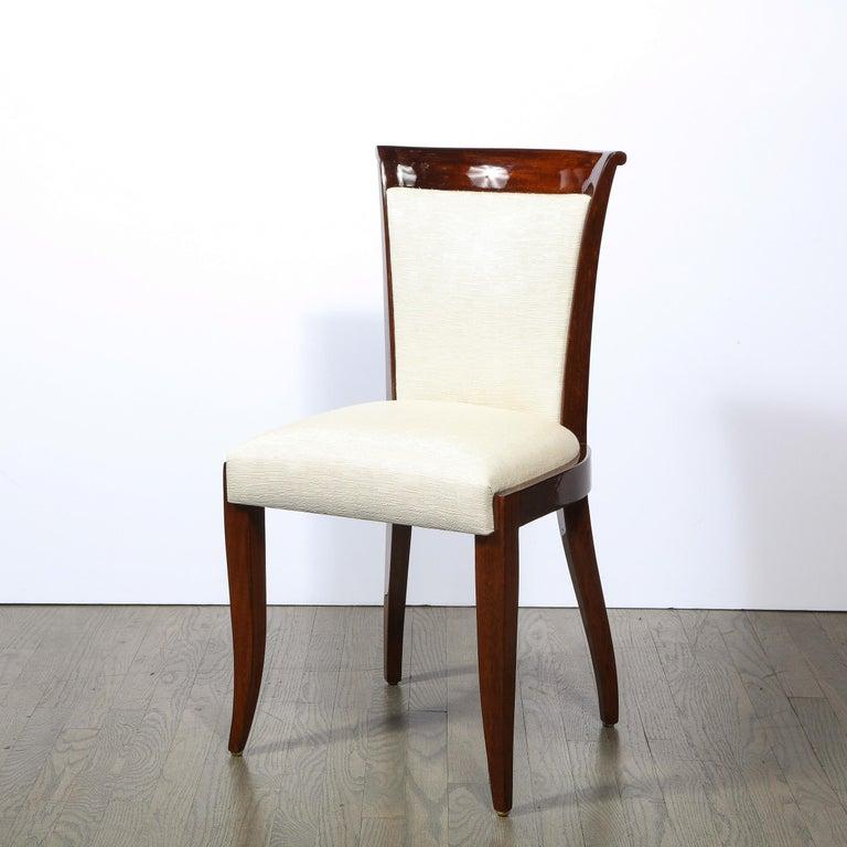 This elegant Art Deco dining chair was realized in France circa 1930. It features a walnut frames with subtle hour back form backs with a slightly cantilevered top; stylized klismos style feet; and newly upholstered backs and seats in Holly Hunt