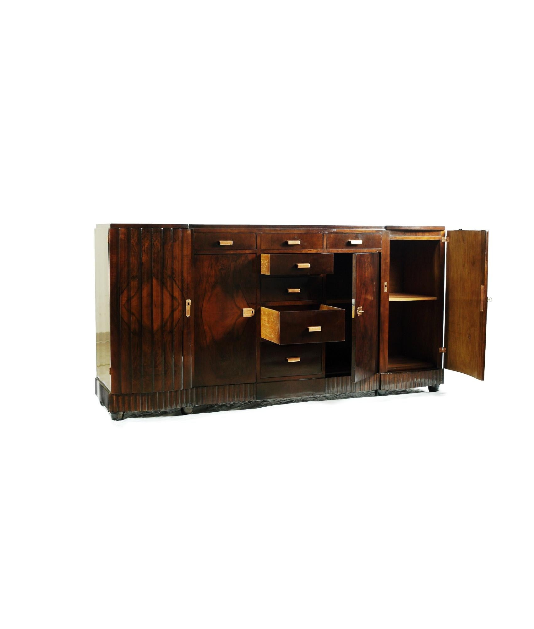 A alluring walnut sideboard, from a single tree veneer, with copper plated
brass handles  and a skilful varnish to last the ages.
All interior sections are clean and finished with four doors, 5 central drawers plus another two side drawers. 
A mid