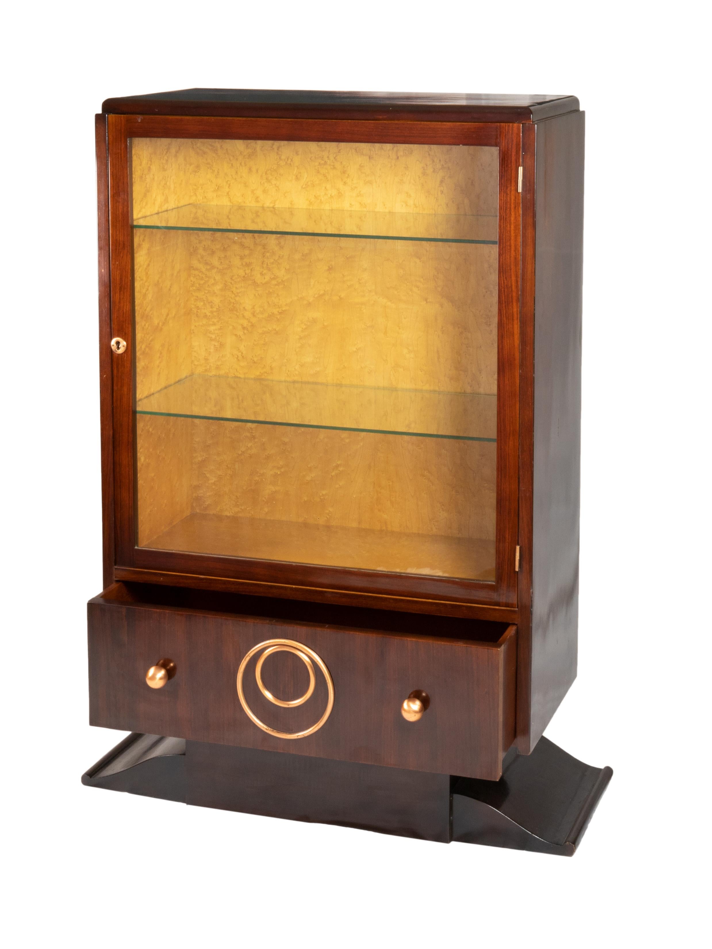Este armario Art Déco de los años 20 ejemplifica la elegancia intemporal de la época. Fabricada en madera de nogal, presenta detalles y asas de cobre que resaltan su diseño geométrico. 
El interior incluye estantes de cristal.

Sus proporciones