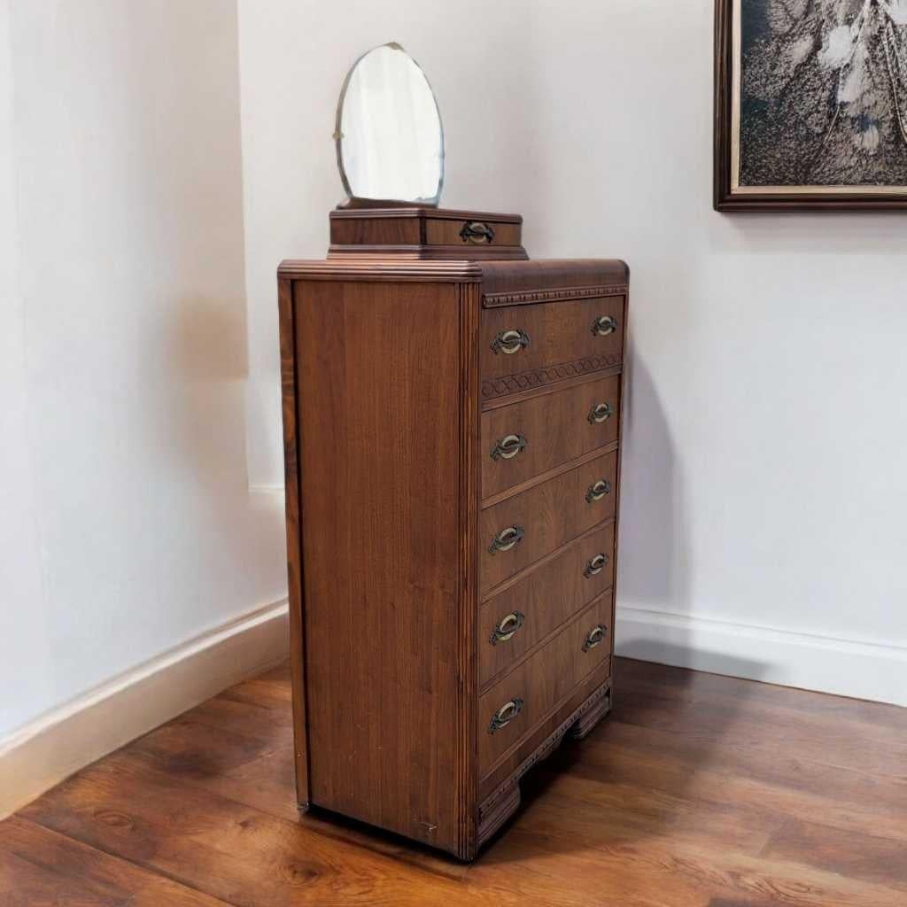 Una cassettiera Art Déco distintiva nella tradizione Wood degli anni '30, realizzata in legno massiccio e con una ricca impiallacciatura con i caratteristici bordi arrotondati e le scanalature verticali. Questo comò alto e stretto unisce il glamour