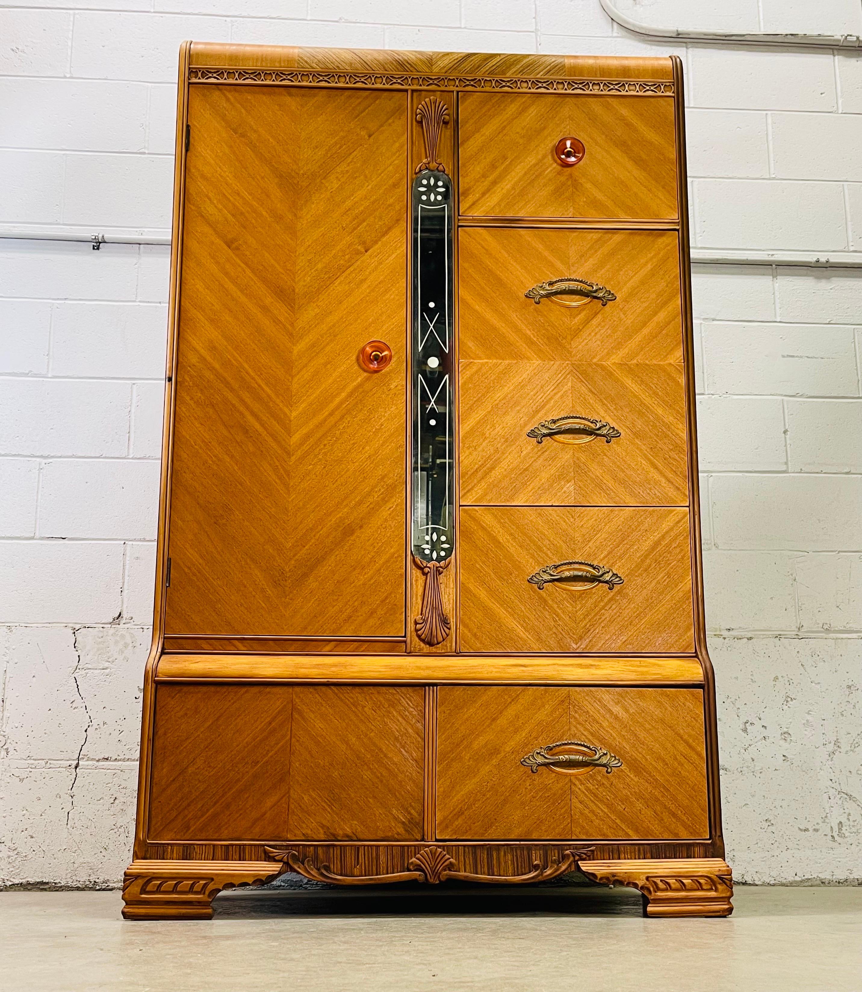 Art Deco tall waterfall style armoire wardrobe. The armoire has a veneer chevron design with accents of zebra wood. The armoire has bakelite pulls and a mirror in the center. All the drawers are 9”H for lots of storage. The cedar lined closet