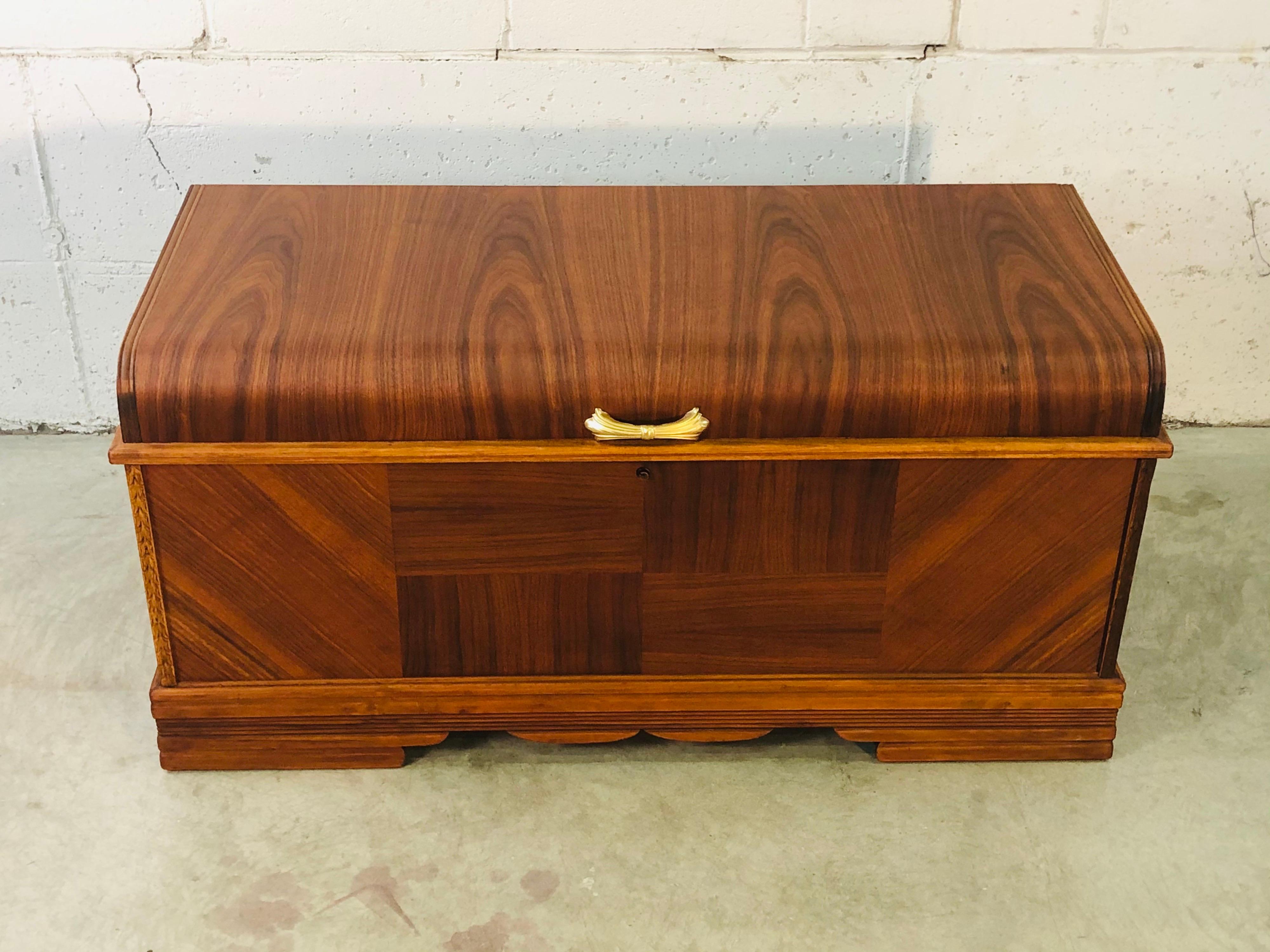 Vintage Art Deco waterfall style cedar blanket chest. The chest has a matchbook veneer finish with gold accent hardware. Cedar lined inside. Marked.