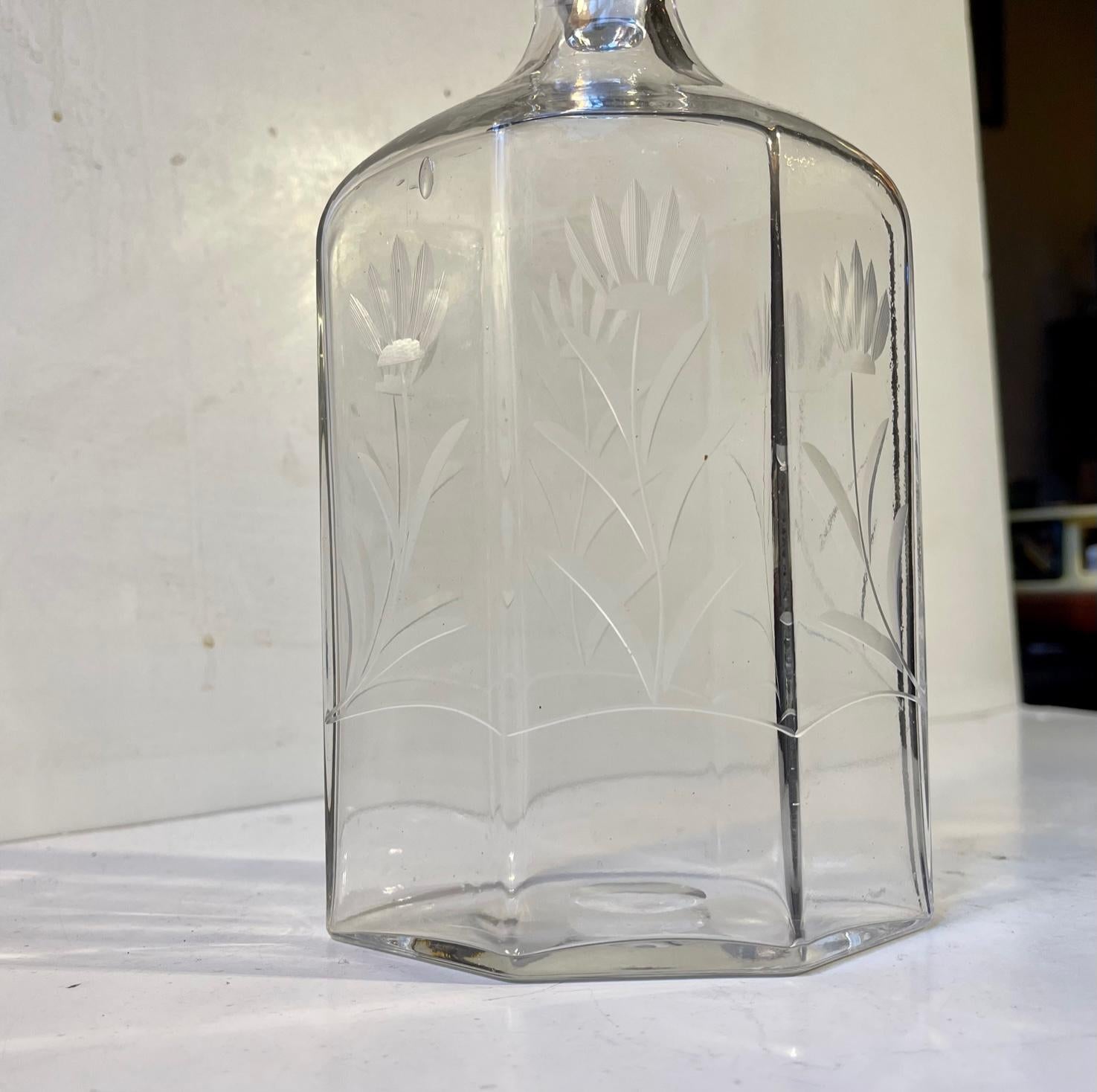 Stylistically strict Art Deco decanter in a hexagonal shape. Its hand-blown in to a mould from clear glass and has hand-etched flowers to all 6 sides and the stopper. Made at Holmegaard Glasværk in Denmark circa 1930-40. Measurements: H: 27 cm, W/D: