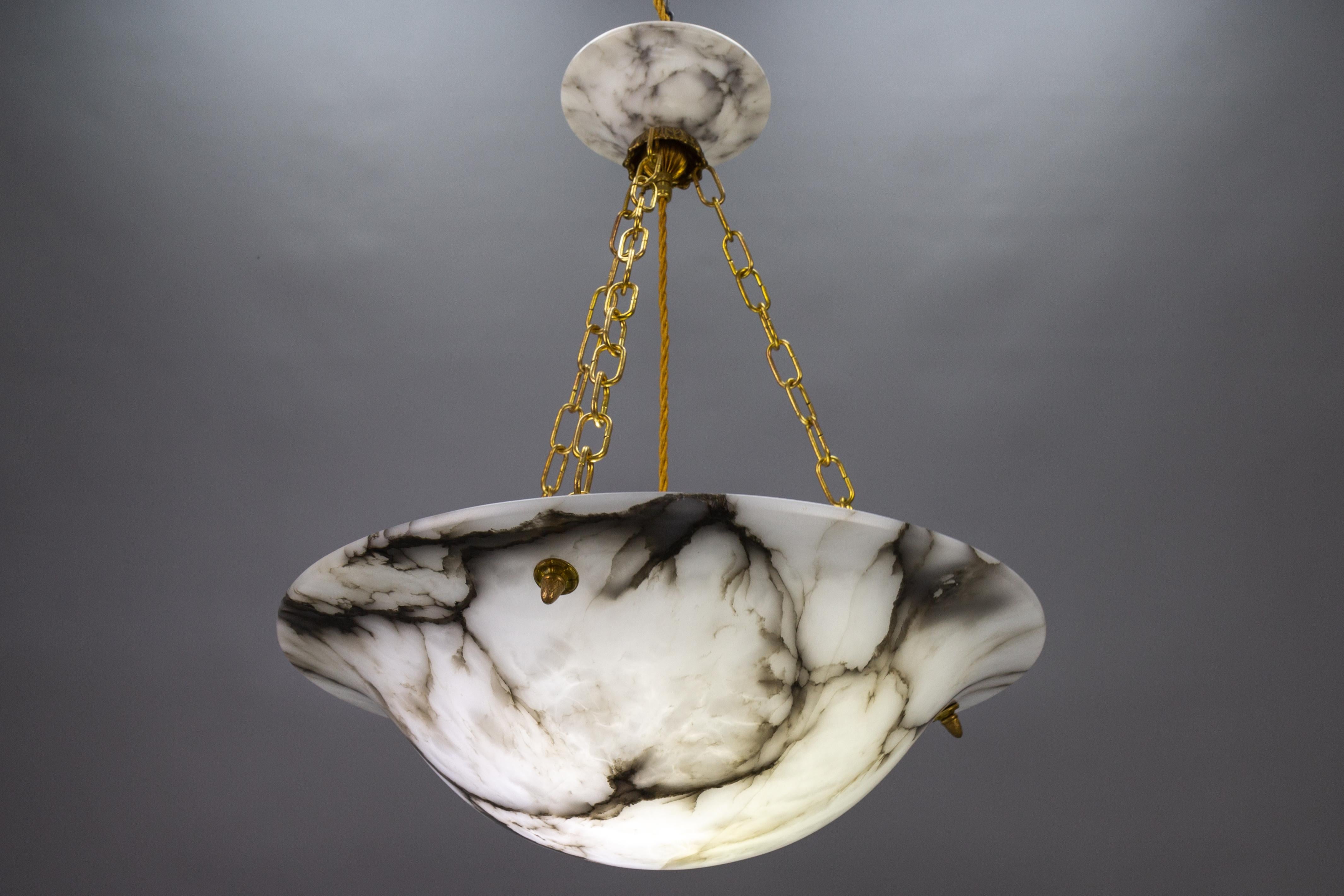 Antique large Art Deco black veined white alabaster pendant light fixture.
Gorgeous and large alabaster pendant ceiling light fixture from circa 1920. Beautifully veined and masterfully carved white alabaster bowl suspended by three brass chains and