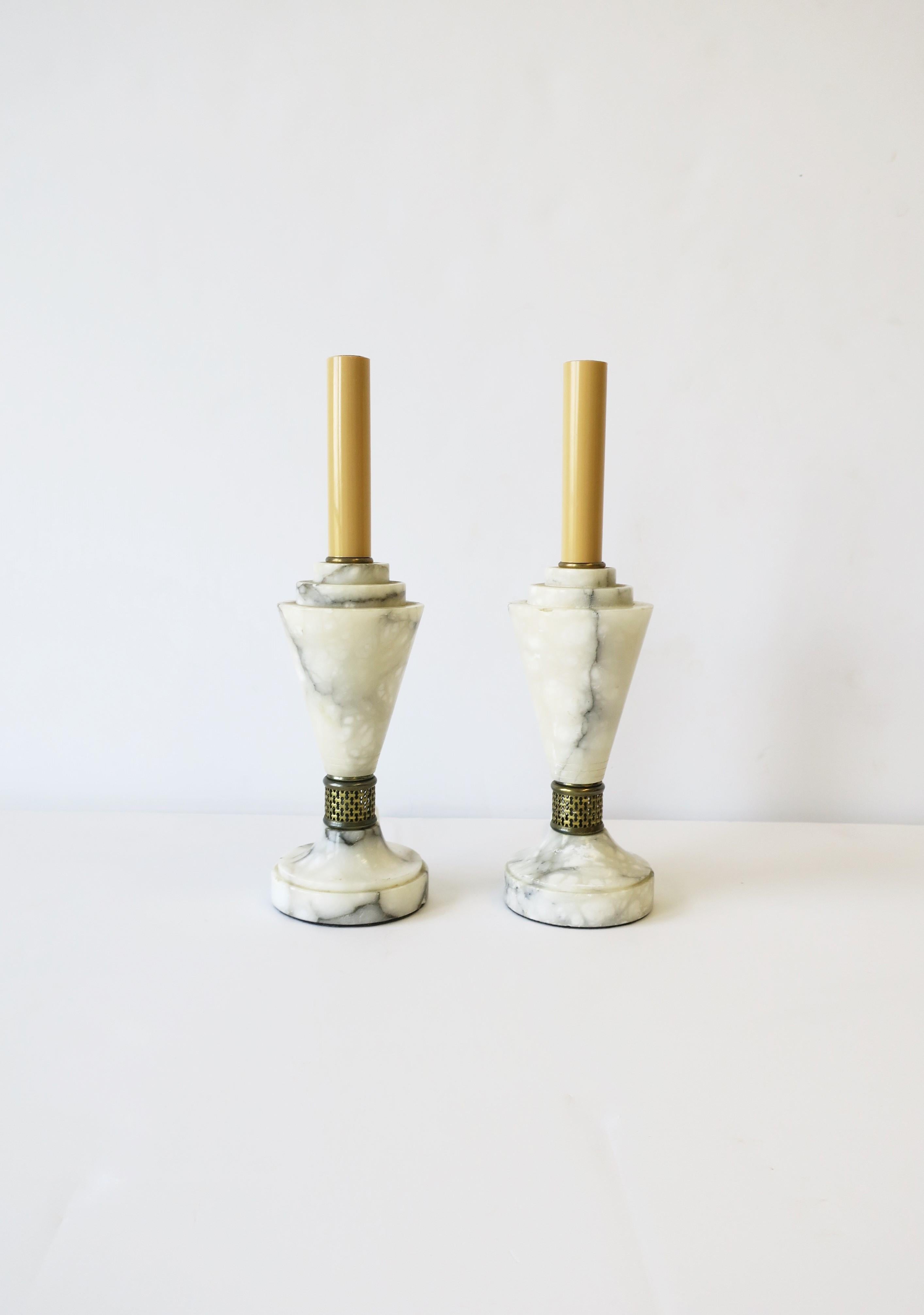 A beautiful pair of solid European Art Deco Modern period Carrara marble table lamps with brass detailing, circa 20th century. Lamps are predominately white marble with black and grey veining. Lamps may be convenient for a table, bedside/nightstand,