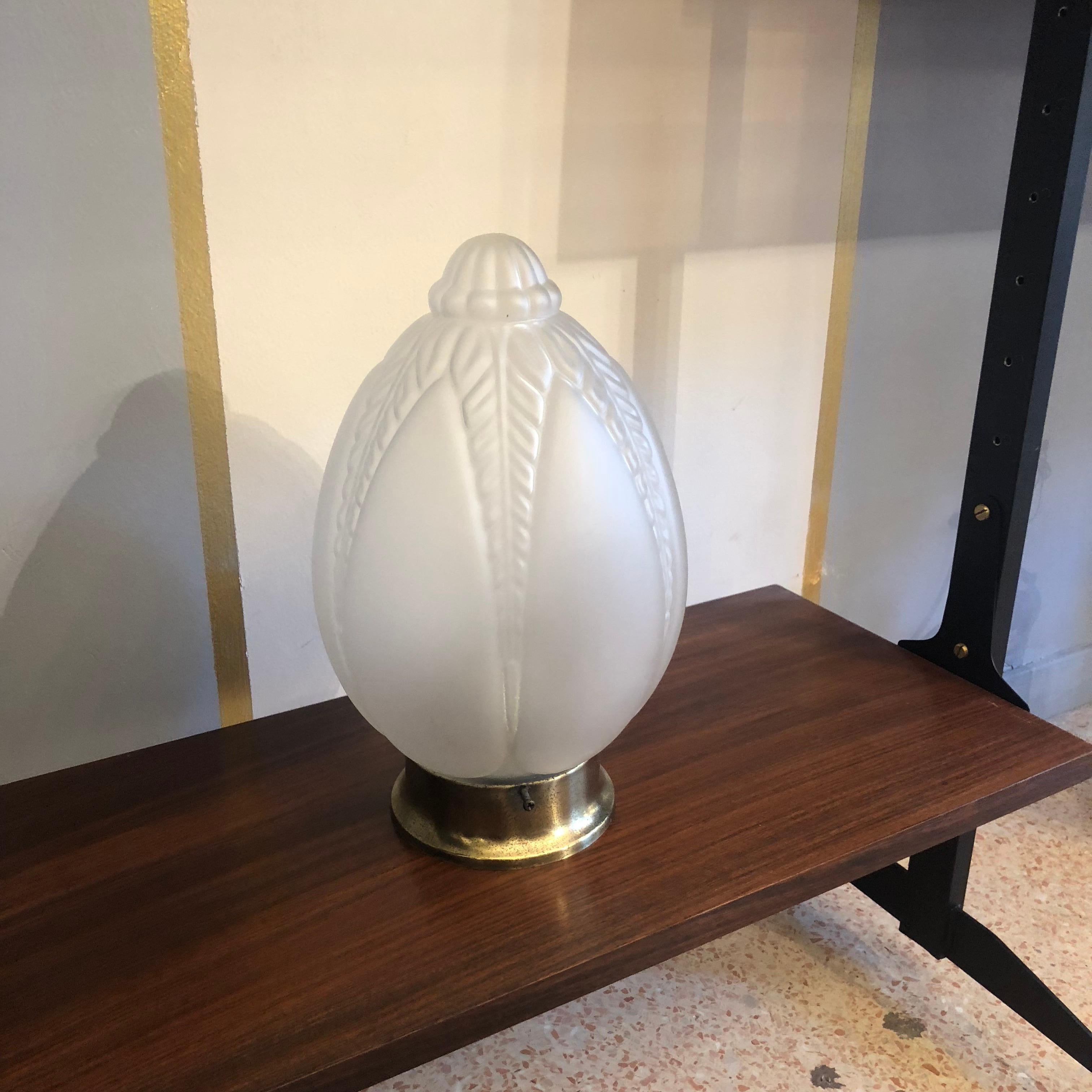 A small lamp that can be used both as table lamp and ceiling lamp. The base is rounded and made in brass, the lampshade is made in white opaque glass. It comes from France from 1930s period the style is absolutely Art Deco with geometrical motif. No