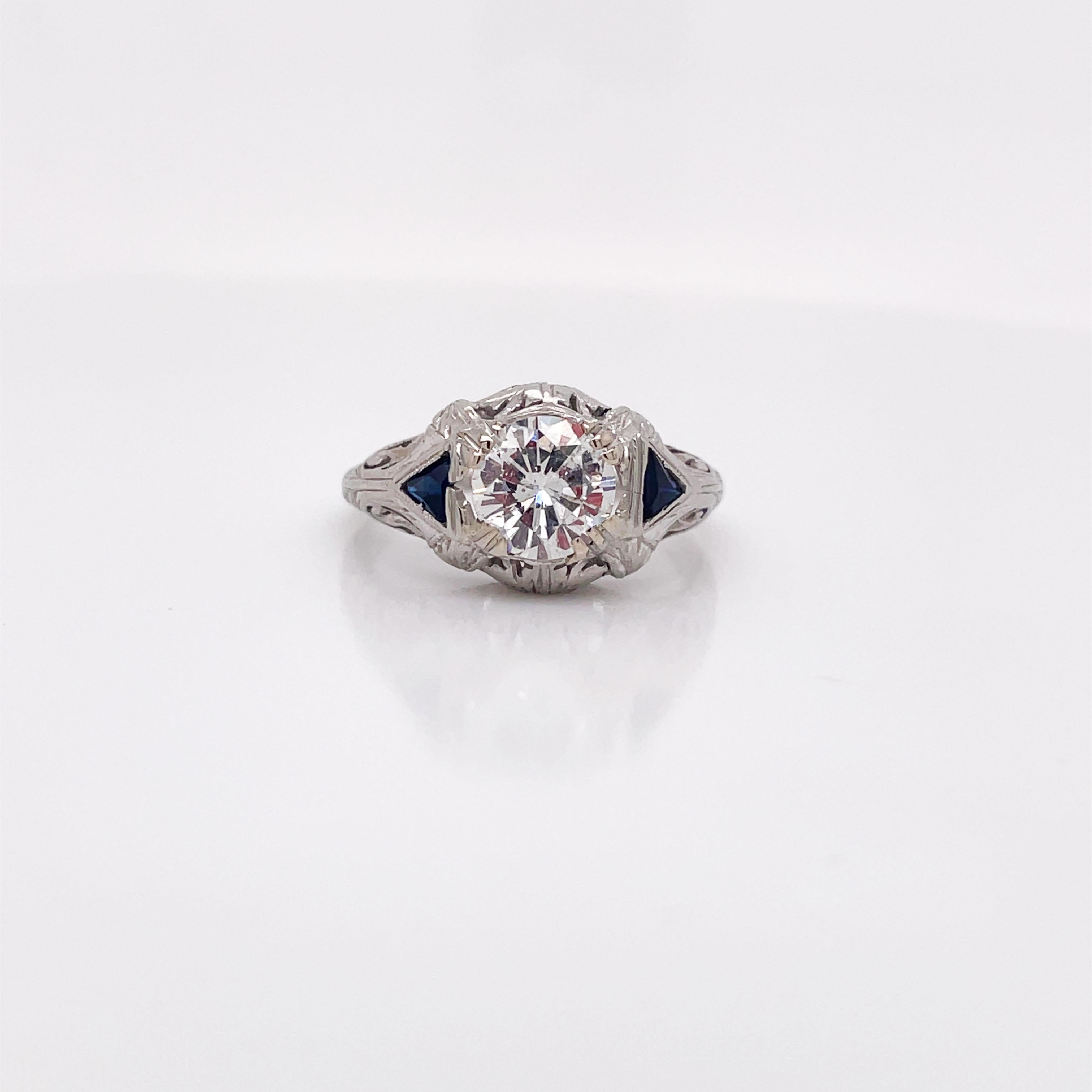 This is an amazing Art Deco diamond and synthetic sapphire ring set in 18K white gold! Adorned with gorgeous and intricate filigree, this ring holds the charm of the Art Deco period. At the center of the ring, is a gorgeous glimmering 0.96ct Euro