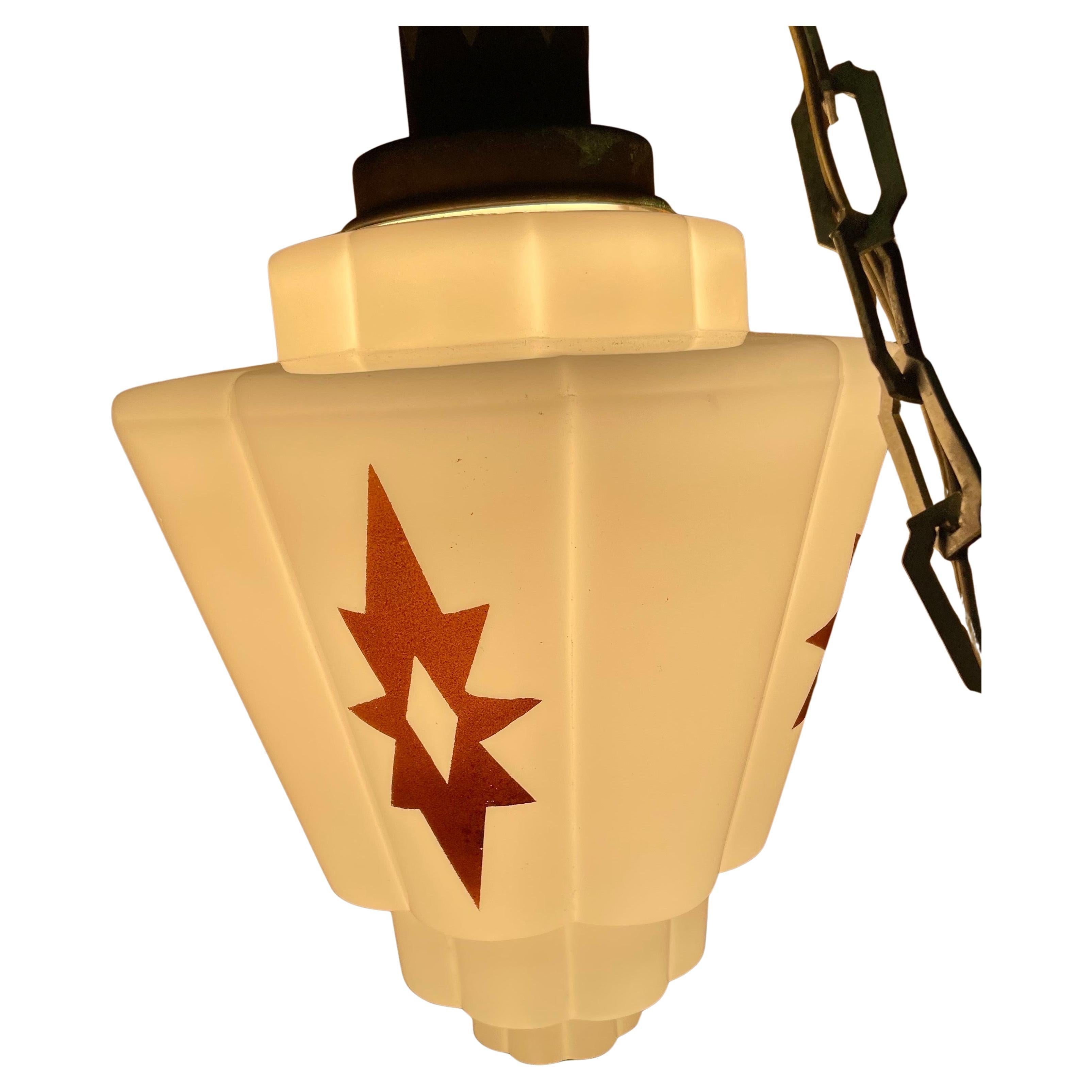 Voici un fantastique luminaire Art déco en verre au lait bulbeux, avec une forme traditionnelle de gratte-ciel incurvé pour le verre et le capuchon en métal. L'abat-jour en verre est décoré d'étoiles de style art déco sur les quatre côtés.