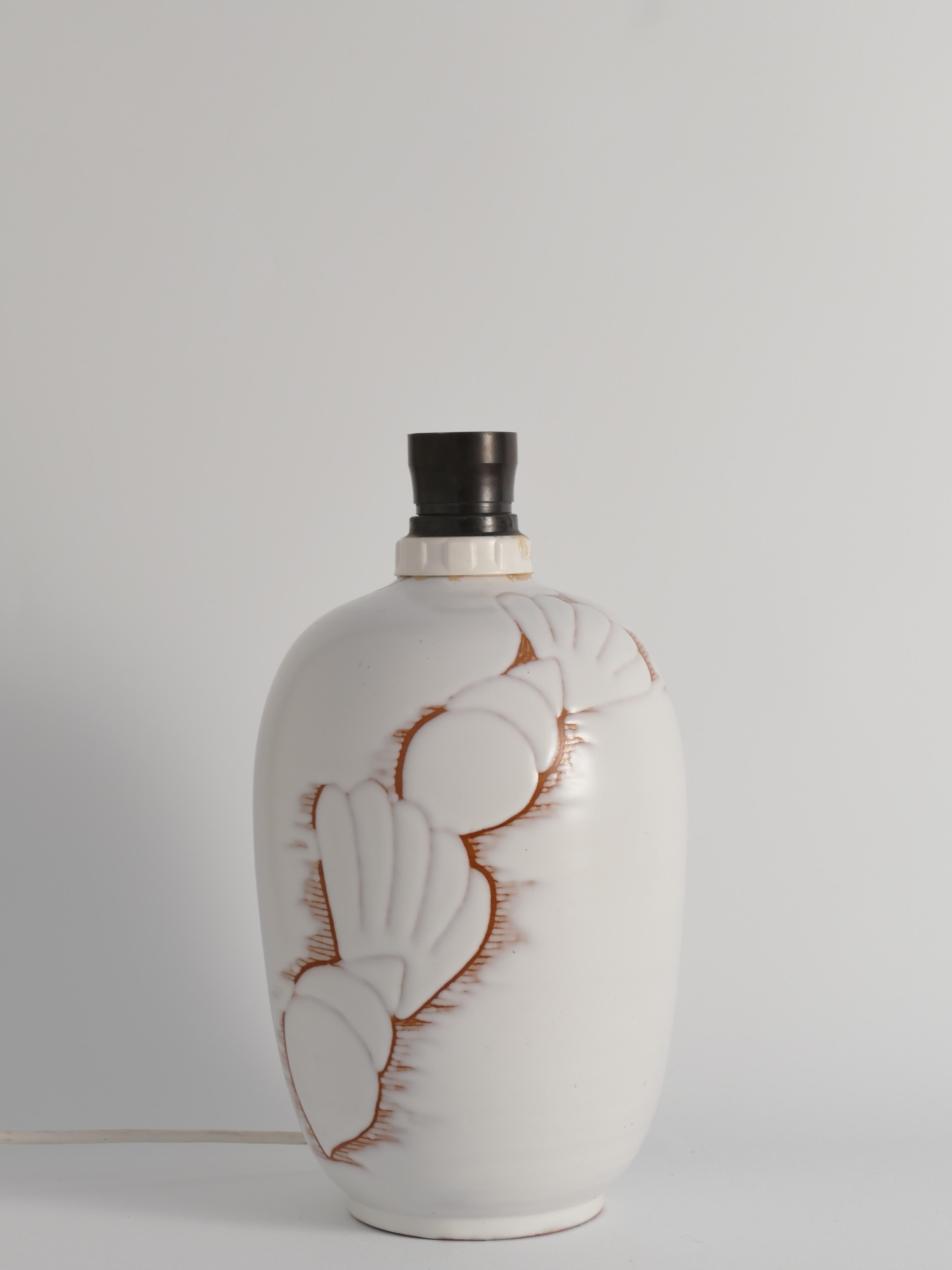 The Snäcka (seashell in Swedish) table lamp, designed by Anna-Lisa Thomson for Upsala-Ekeby in the 1940s, is a stunning example of Swedish mid-century ceramic artistry. Made of earthenware with a matte white glaze, the lamp features an elegant