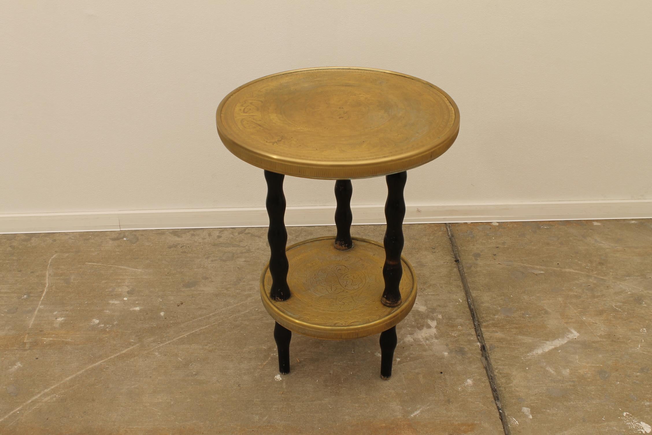 This side table was made around the 1930s and has a wooden structure, turned wavy walnut wooden legs painted black. The round table top is made of brass with engraved decorative motifs.
The table has a nice patina and is in its original,