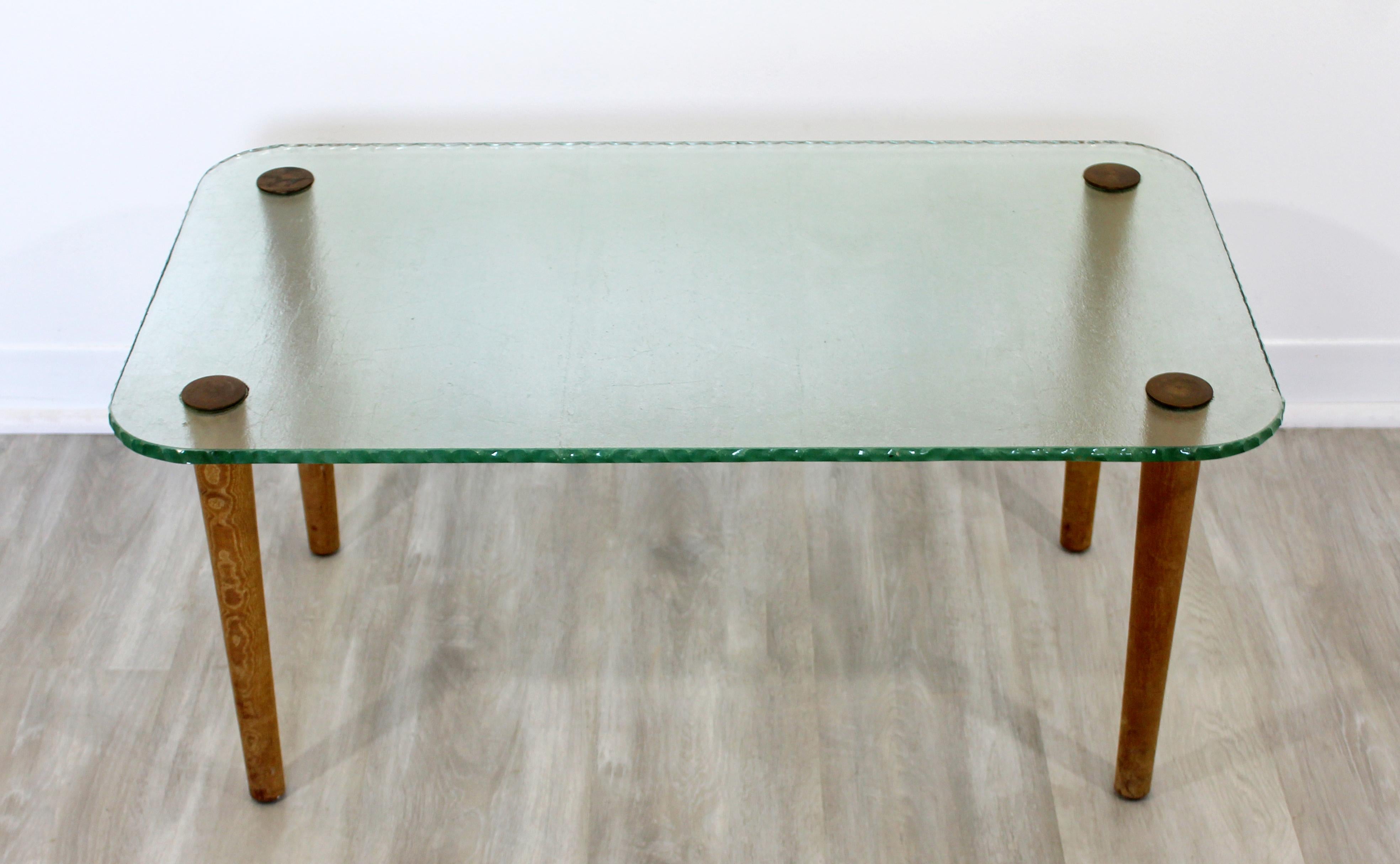 For your consideration is a gorgeous coffee table, with a rectangular, tempered chipped edge glass top on wood legs with bronze caps, in the style of Gilbert Rohde, circa 1940s. In excellent antique condition. The dimensions are 34