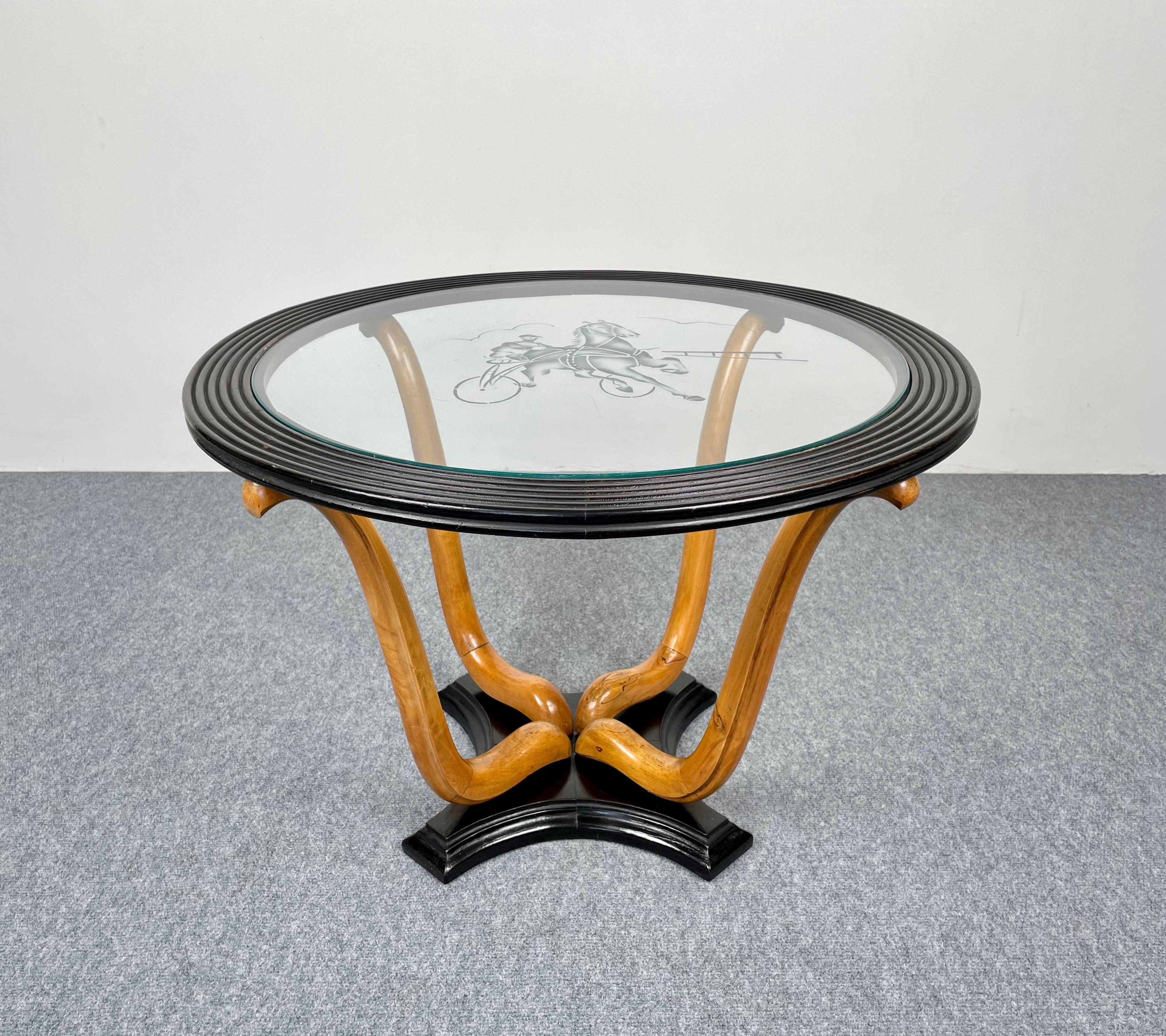 Round coffee side table featuring four hand-carved curved legs of a lighter wood on a dark wood base. The glass top is decorated with a frosted glass jockey on his horse and is framed by concentric dark wood. Made in Italy in the 1940s.