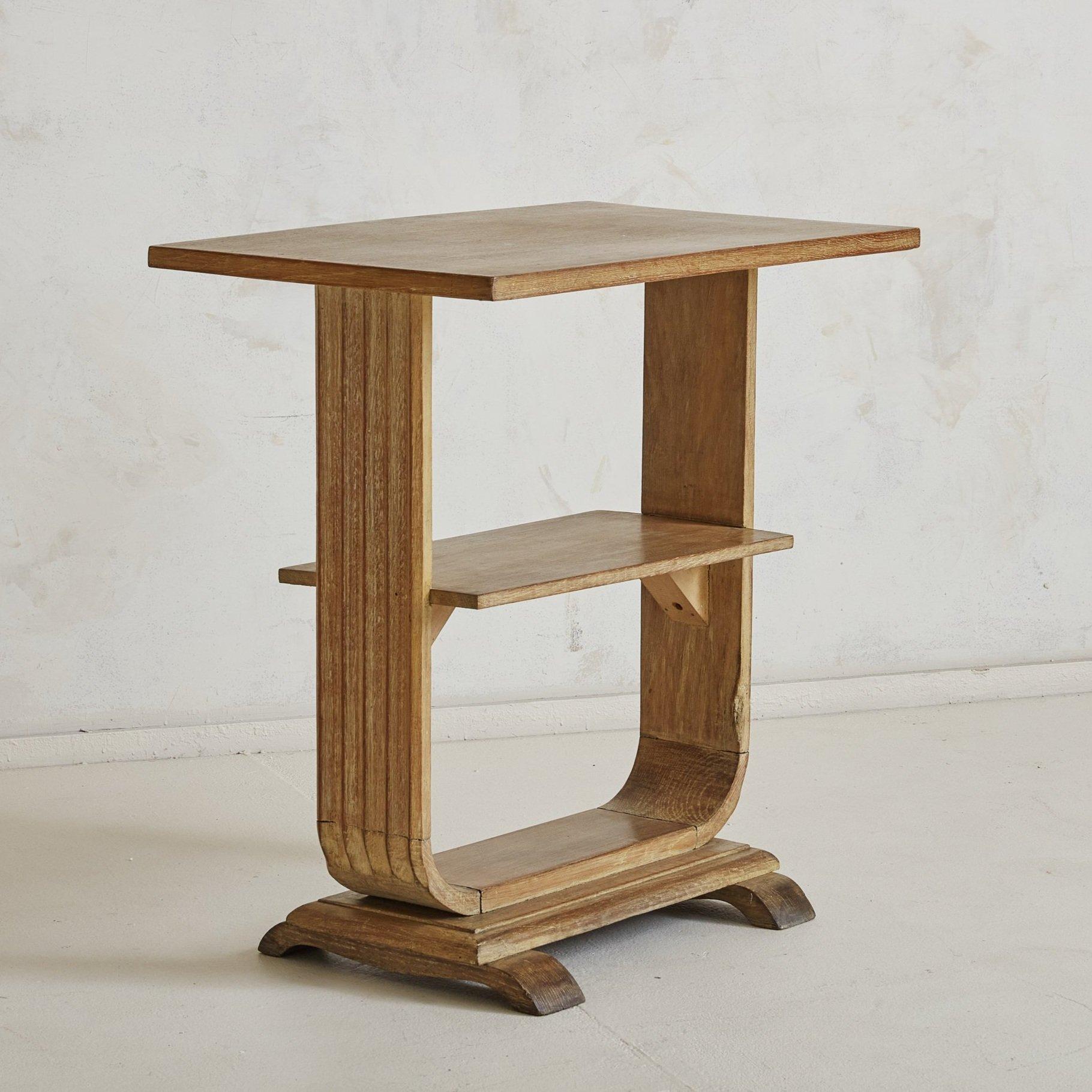 A French Art Deco small wood side table from the 1940s. This side table features three rectangular shelves, a “U” shaped tulip frame with column detailing, and two curved legs at the base. The wood has textured graining throughout with varying