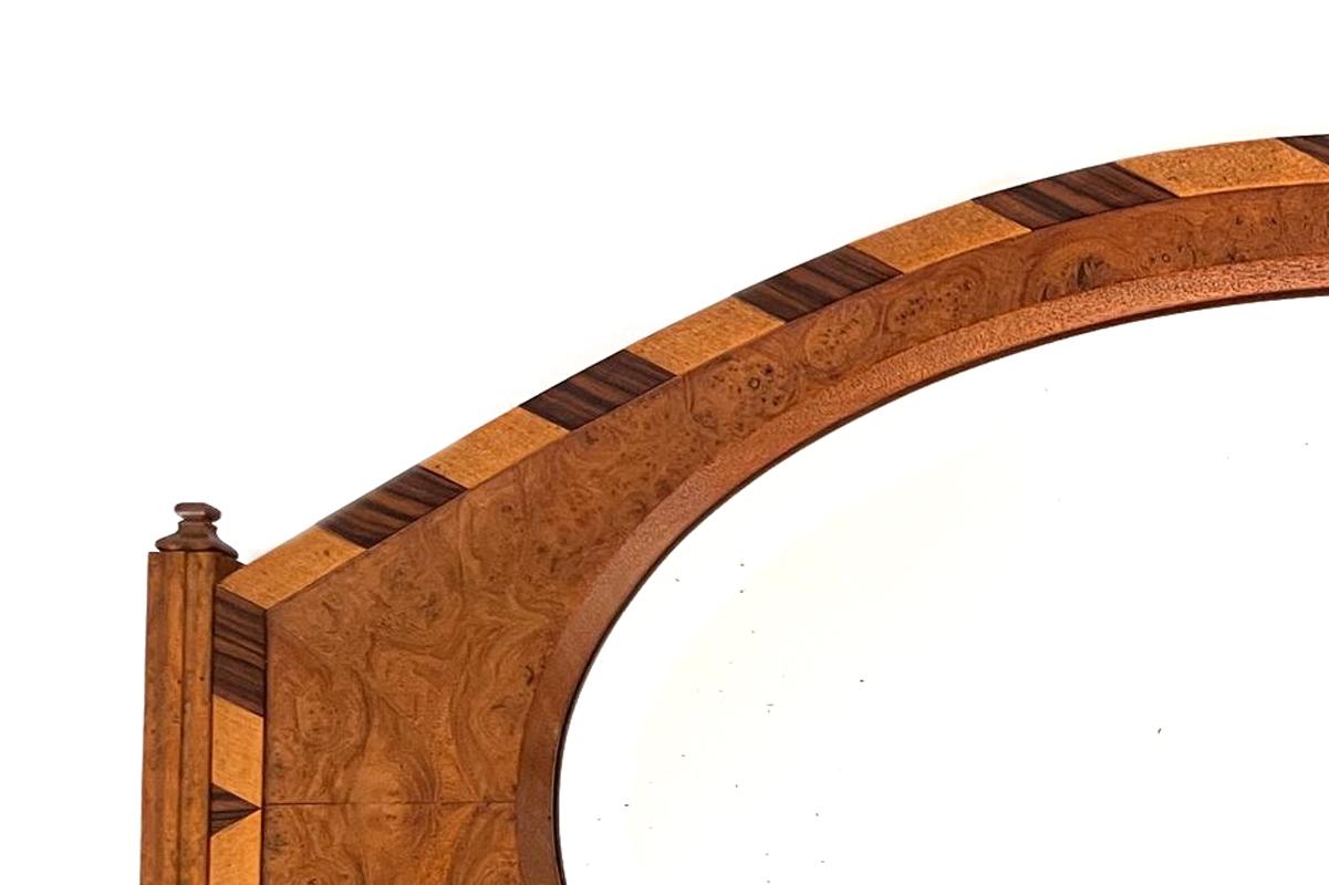 Questo bellissimo specchio da appendere in stile Art-Déco è realizzato con dettagli meticolosi. Il pezzo presenta un vetro ovale di grande effetto incastonato in una cornice di legno riccamente decorata con impiallacciatura e intarsio. La simmetria