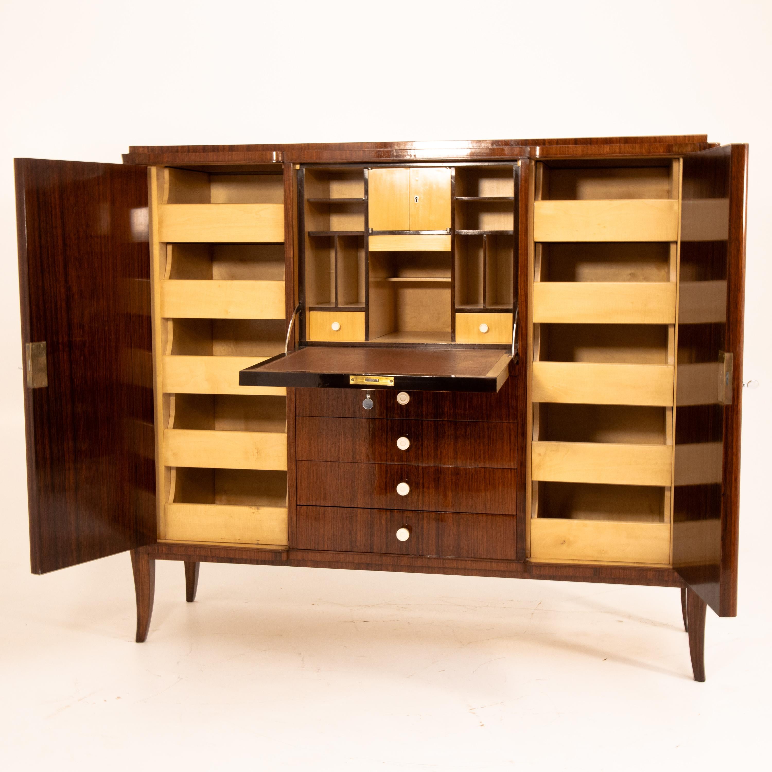 Art Deco cabinet standing on elegantly curved legs with two side doors, four drawers and a central writing flap. Behind the doors there are pull-out drawers; the writing flap accommodates pigeonholes and small drawers and is covered with red