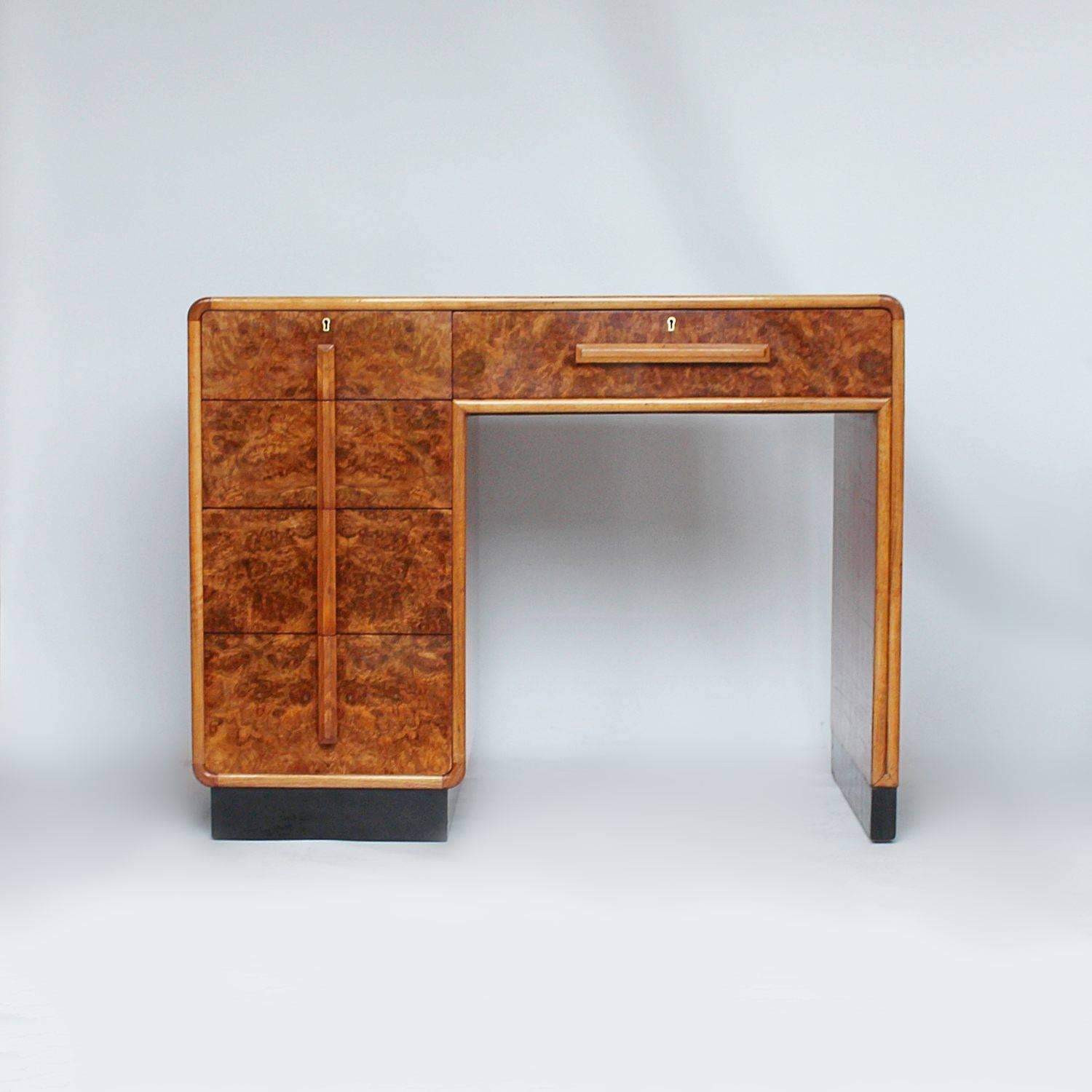 An Art Deco writing desk with four side drawers and central drawer in burr walnut. Straight grain walnut veneer to side and back. Desk sits atop ebonised base. Original wooden handles and original tan leather top.



     