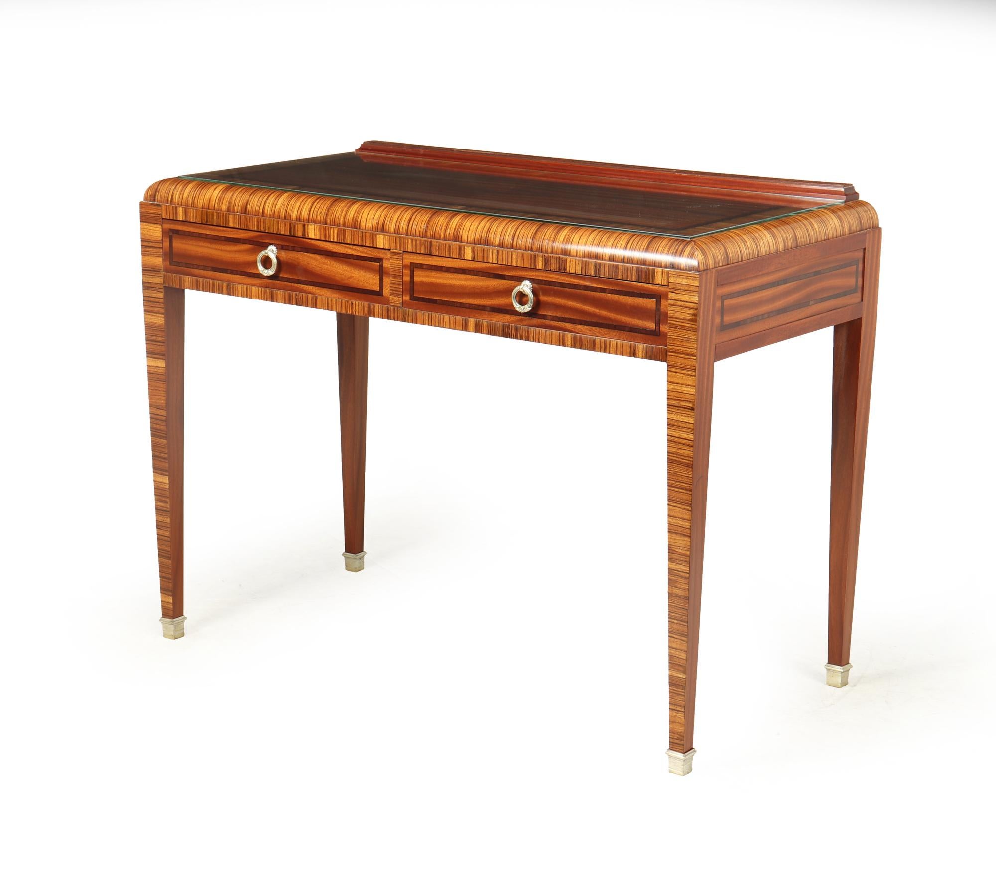 A French Art Deco Writing table produced in zebrano and Sapele with ebony inlay in France in the 1930’s, it has bronze hoop drop handles and silver gilt bronze sabots it has a set in glass plate top

Age: 1920

Style: Art Deco

Material: