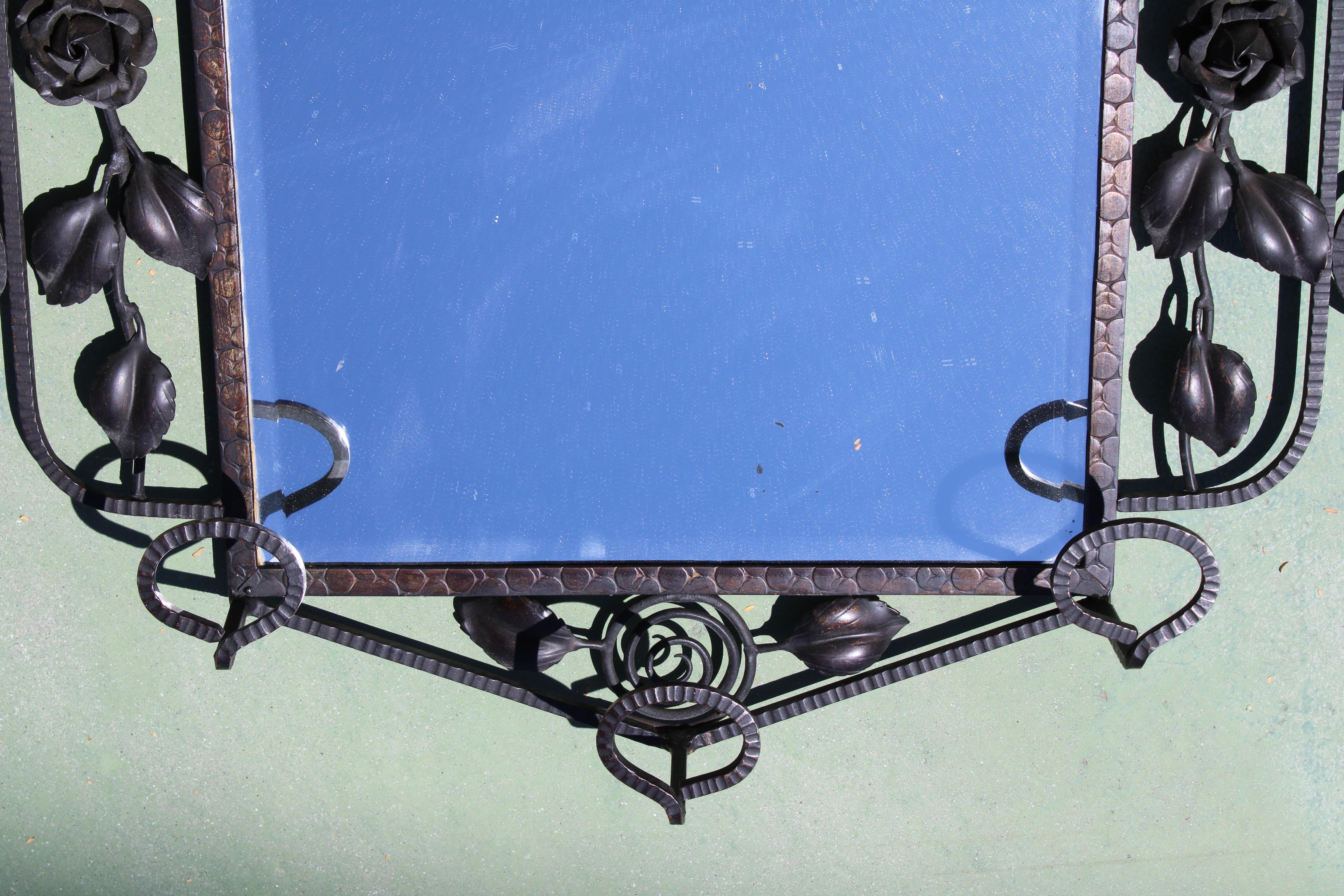 Miroir Art Déco en fer forgé avec une étagère au-dessus et des crochets à chapeau en dessous. Des formes florales stylisées ornent chaque côté. Le miroir biseauté mesure 11