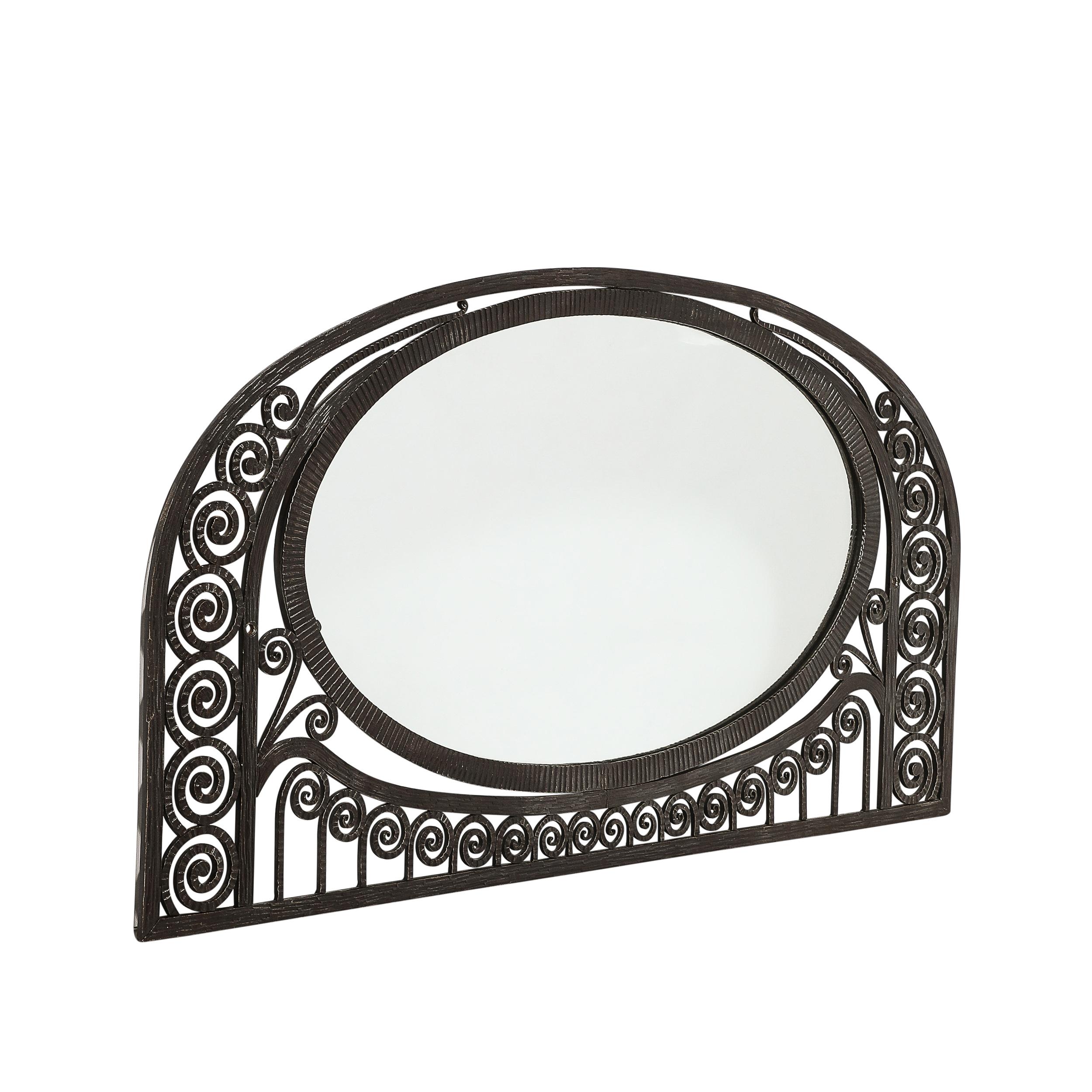 This elegant Art Deco wrought iron mirror was realized in the manner of Edgar Brandt in France, Circa 1930. It features scroll form detailing which resembles the tightly coiled fronds of fiddle head ferns, circumscribing a horzontally oriented oval